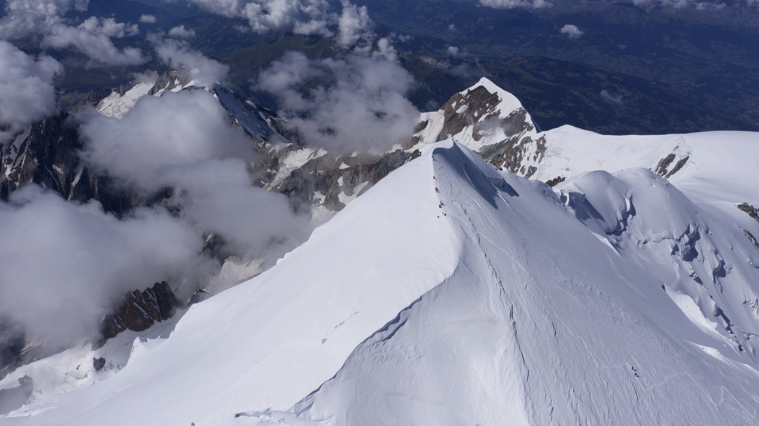 Snow-covered mountain ridge with rocky peaks and clouds in the sky.