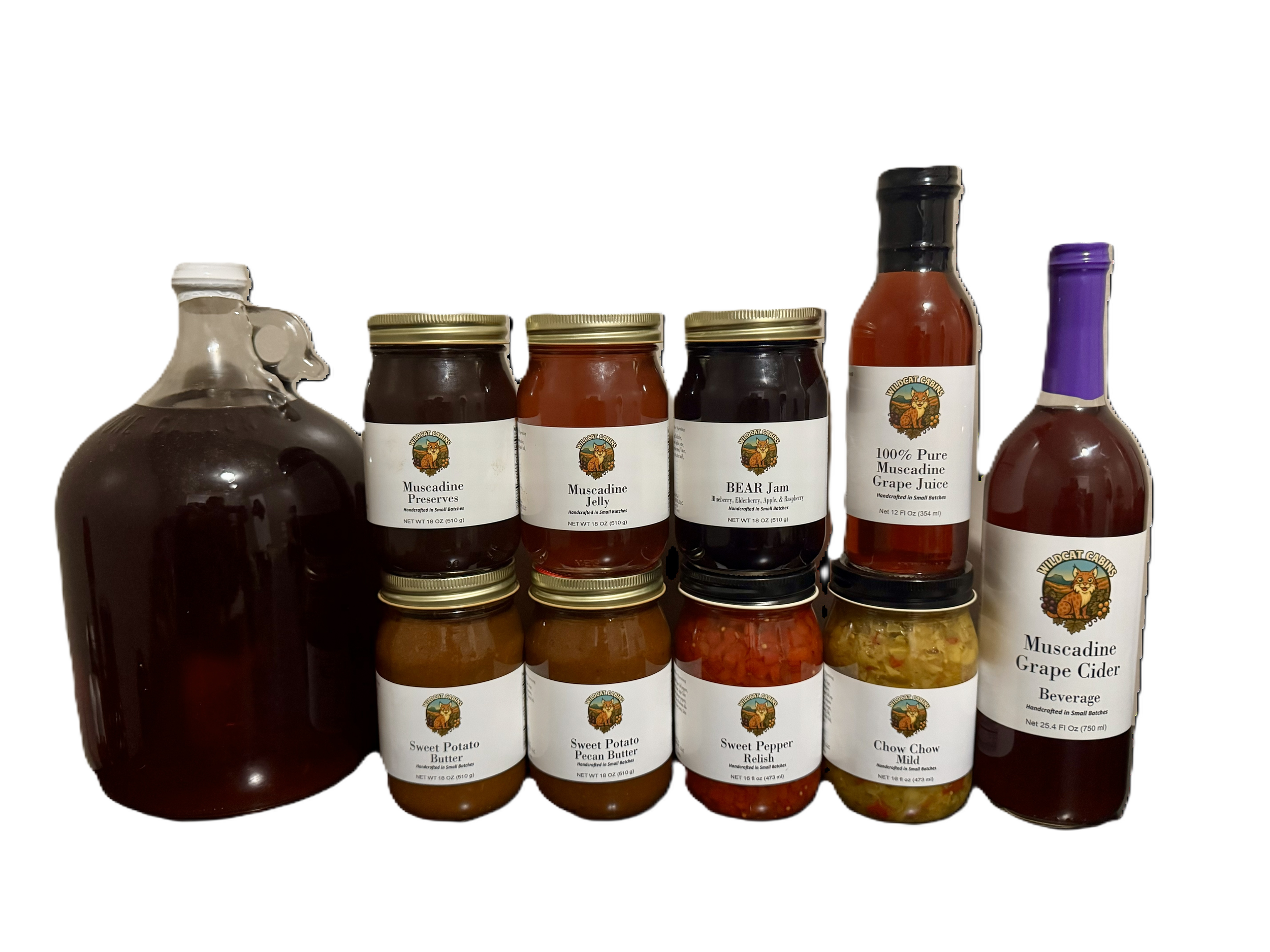 Variety of homemade jams, preserves, sauces, and beverages labeled with Wildcat Cabin logo, including Muscadine preserves, jelly, bear jam, grape juice, grape cider, sweet potato butter, sweet potato pecan butter, sweet pepper relish, and chow chow, arranged on a table.