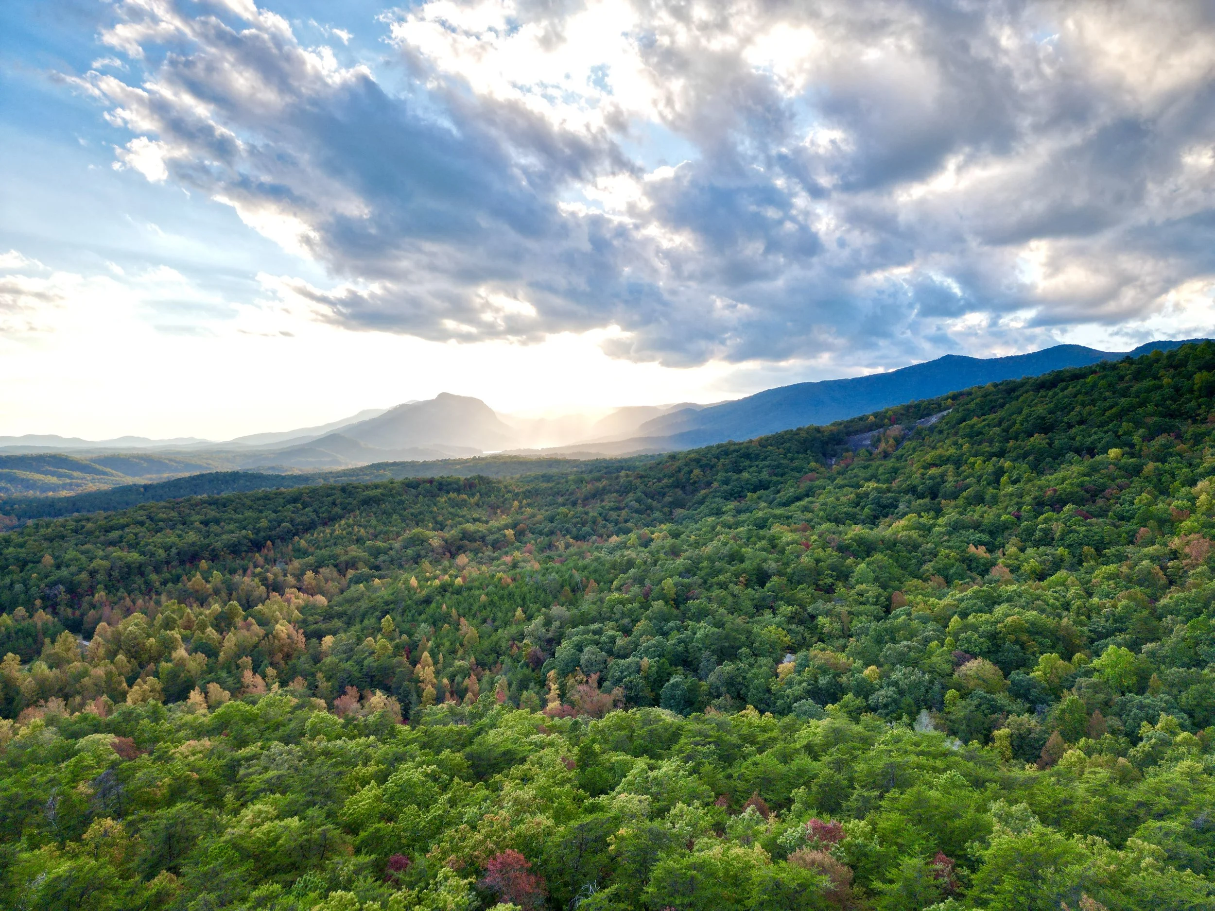 Scenic view of green forested mountains at sunset with partly cloudy sky.