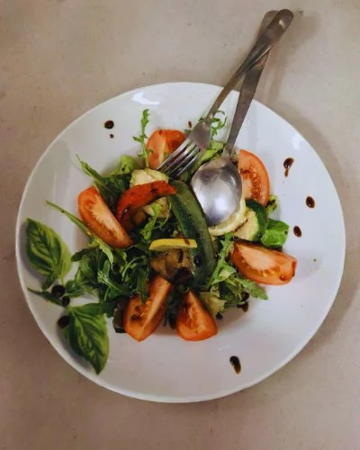Salade met tomaten, komkommer, sla en balsamico dressing op een wit bord, met een vork en lepel erop.