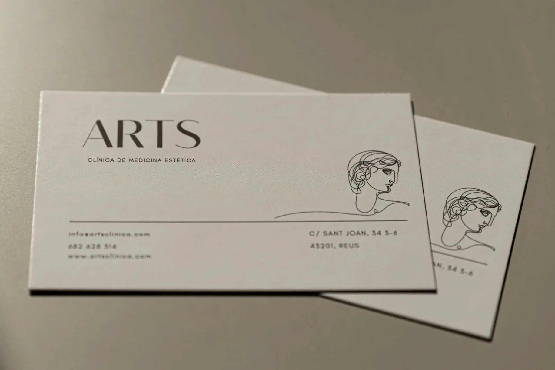 Tarjetas de presentación blancas para una clínica de medicina estética llamada ARTIS, con dibujo de perfil de mujer y dirección en Reus.