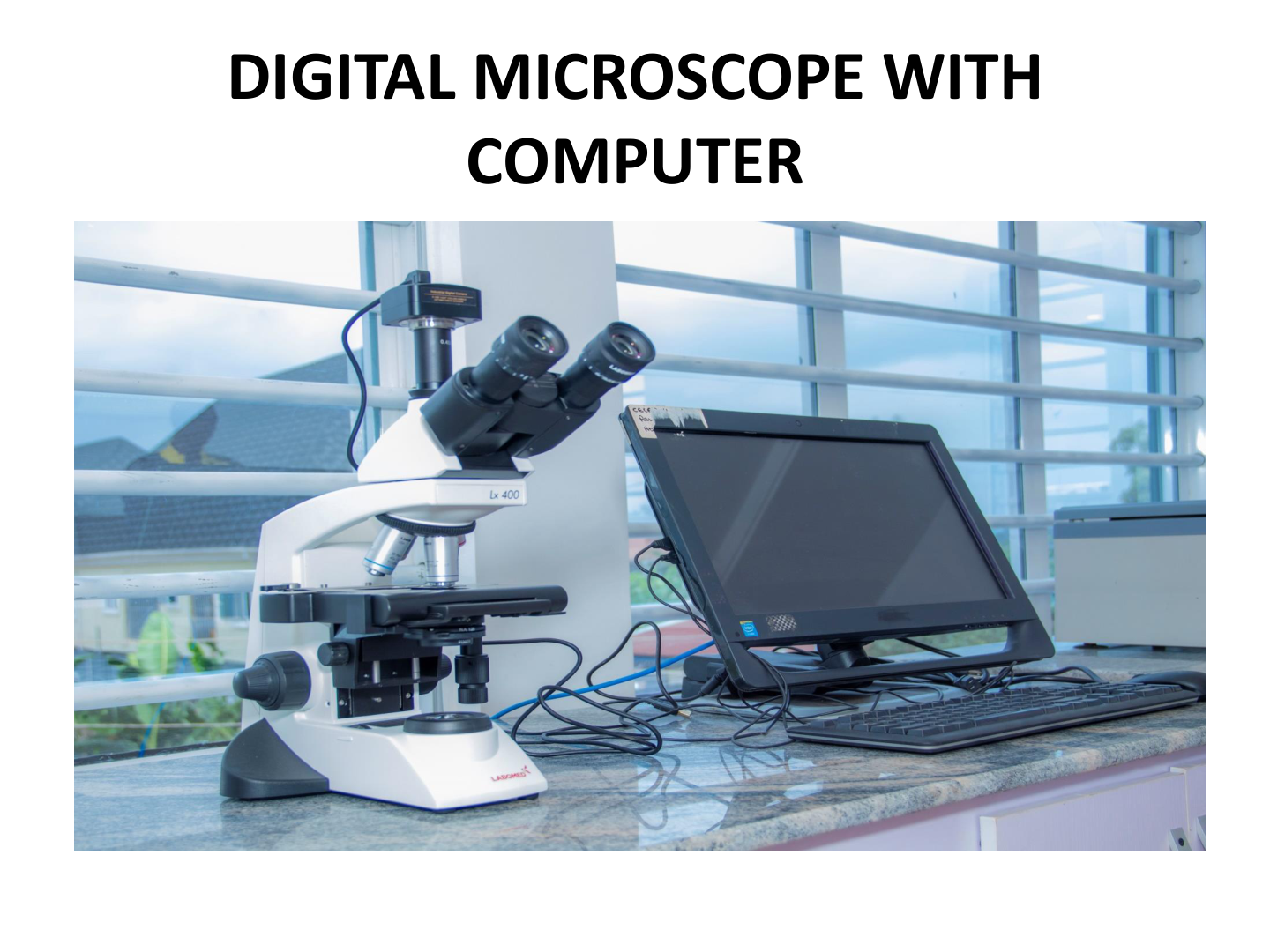 A microscope connected to a computer on a lab counter with windows in the background.