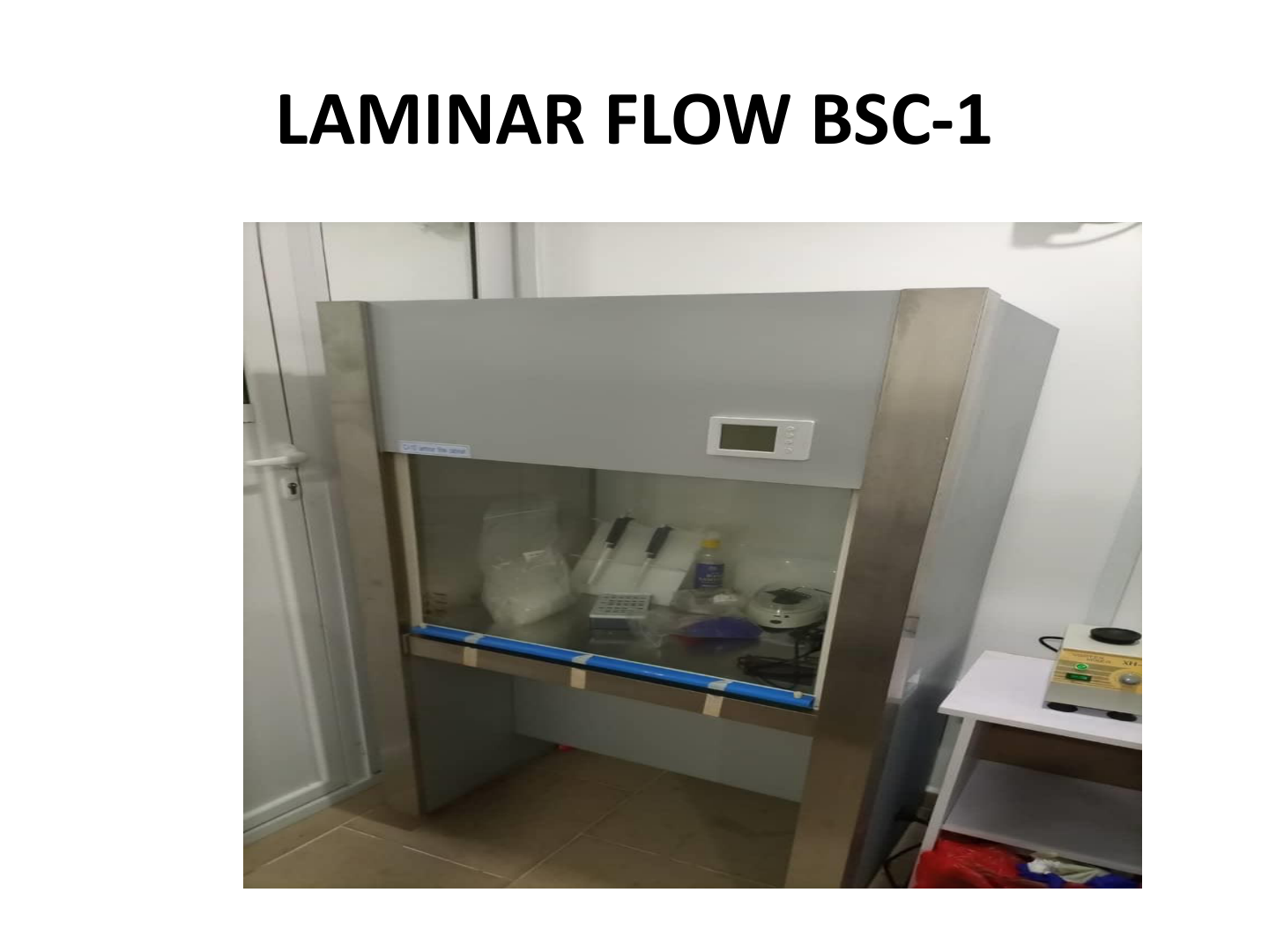 BSC-1 laminar flow hood in laboratory with items inside, including a calculator, bottles, and plastic containers.