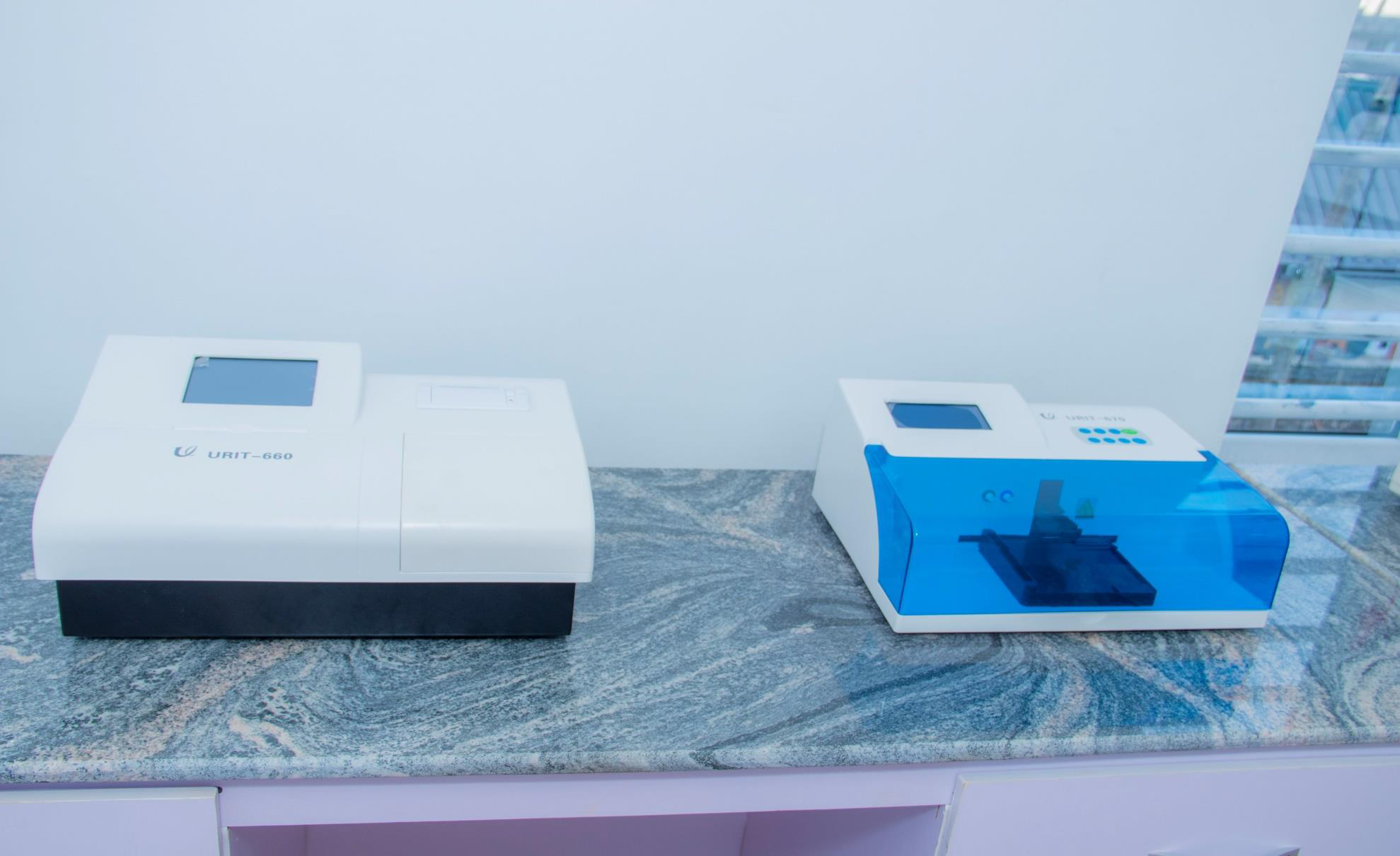 Two laboratory instruments on a marble countertop, one labeled 'URIT-660' with a white and black body, and the other with a white body and a blue transparent cover, each with a touchscreen display.