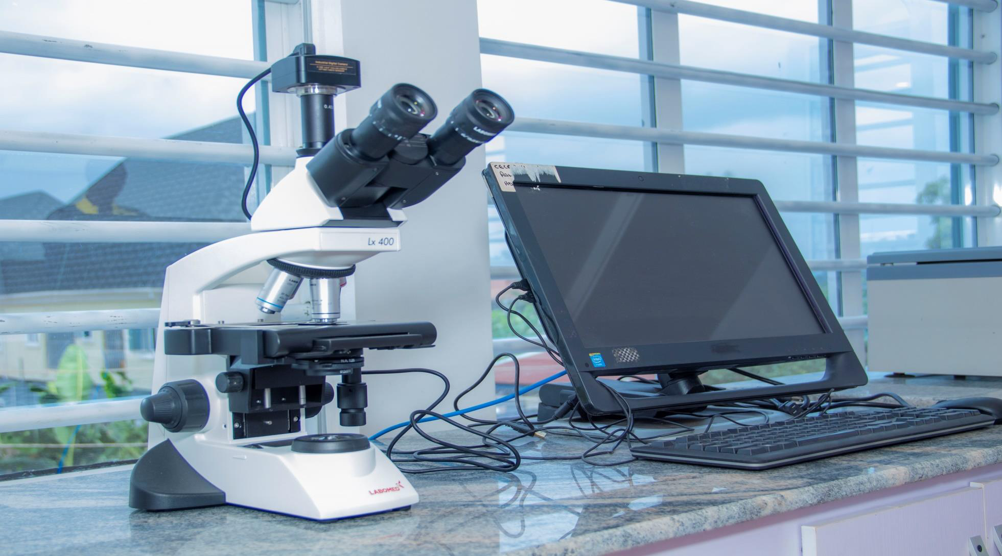 Microscope and computer on laboratory countertop near window.