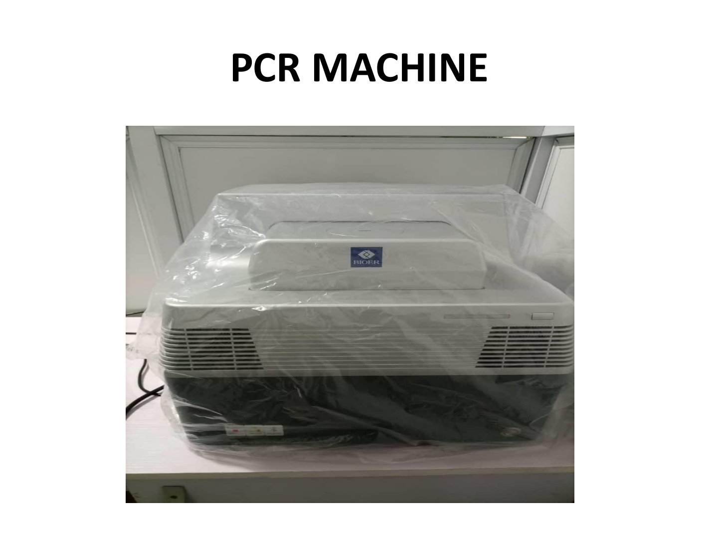 A PCR machine with a Bioer logo, covered in clear plastic, placed on a white table in a laboratory setting.