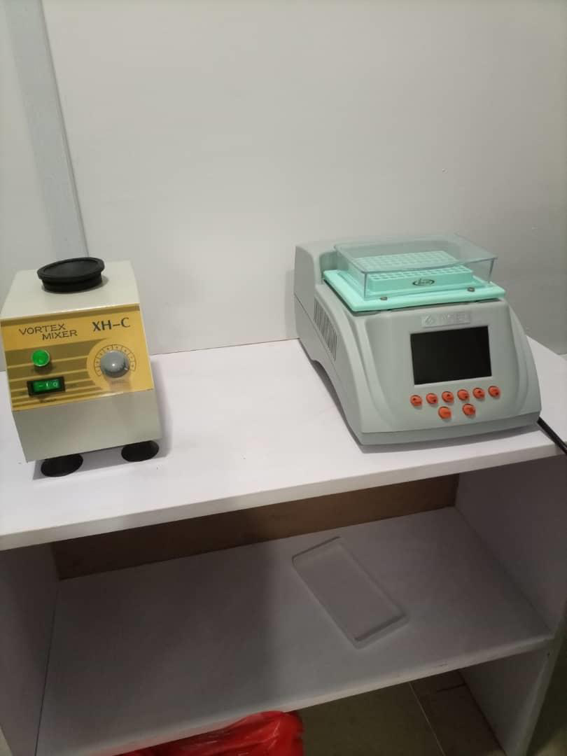 Laboratory equipment on a white table, including a small Vortex mixer and a centrifuge with a digital display.