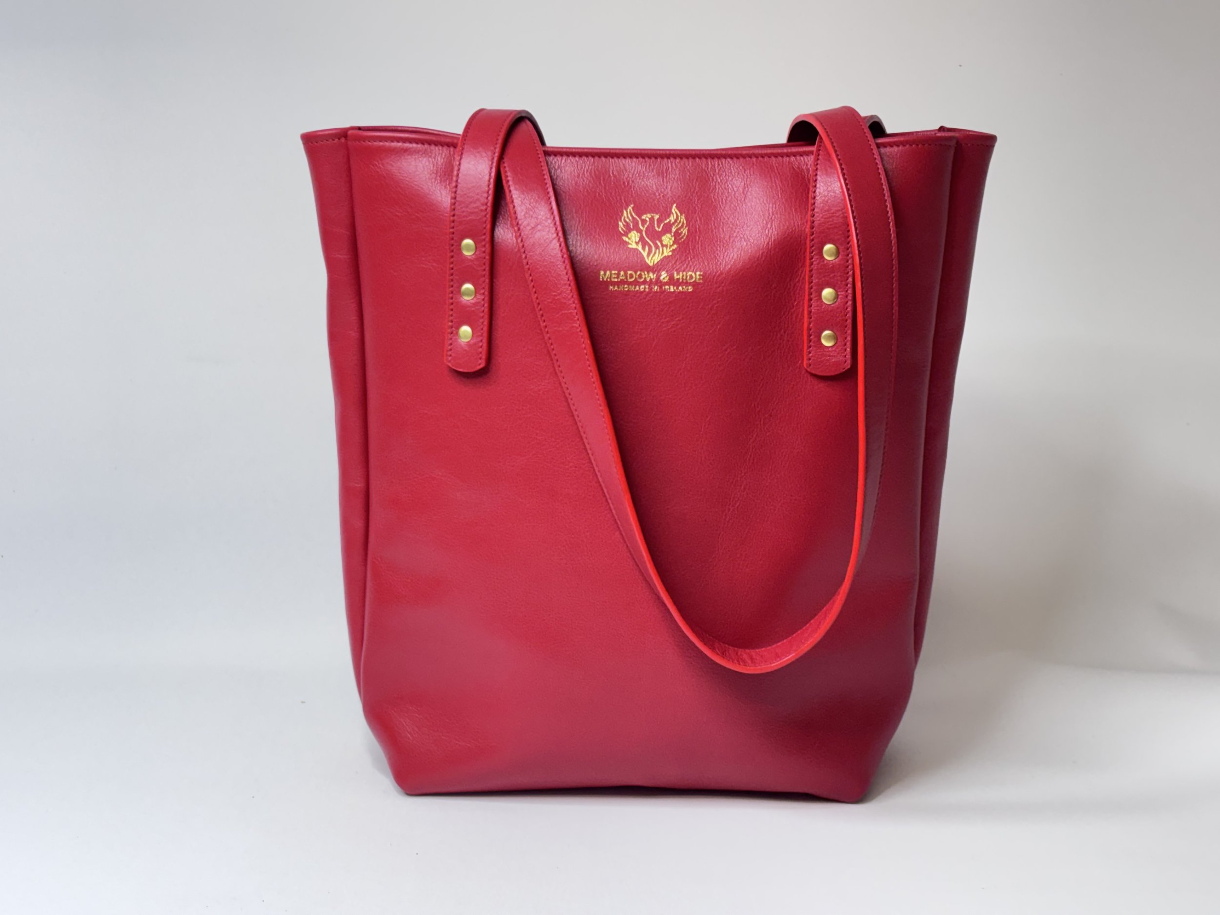 A black handbag with a leopard print clutch and gold hardware, bearing the Meadow & Hide logo in gold on the front