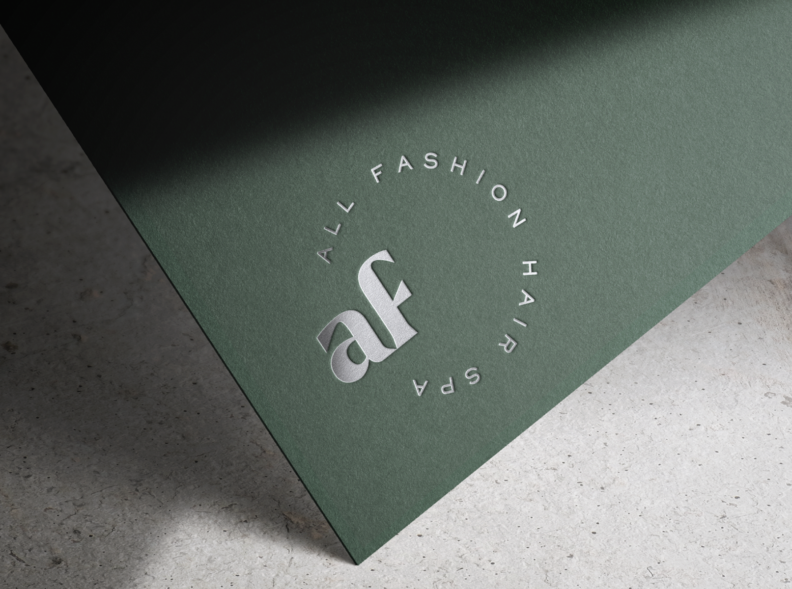 Close-up of a dark green textured paper with a silver embossed monogram of a hair spa.