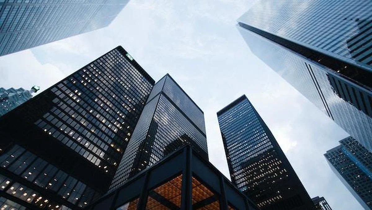 View of tall glass skyscrapers from ground level, looking up at overcast sky.