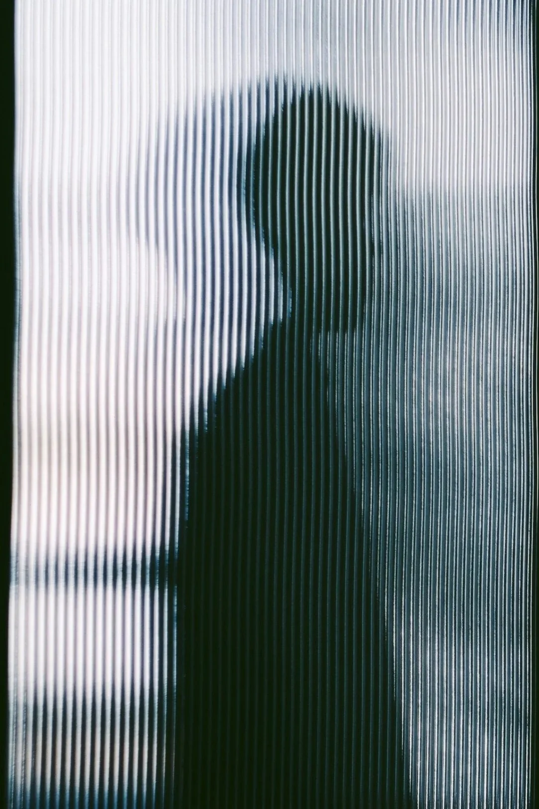 Silhouette of a woman seen through frosted, ribbed glass.