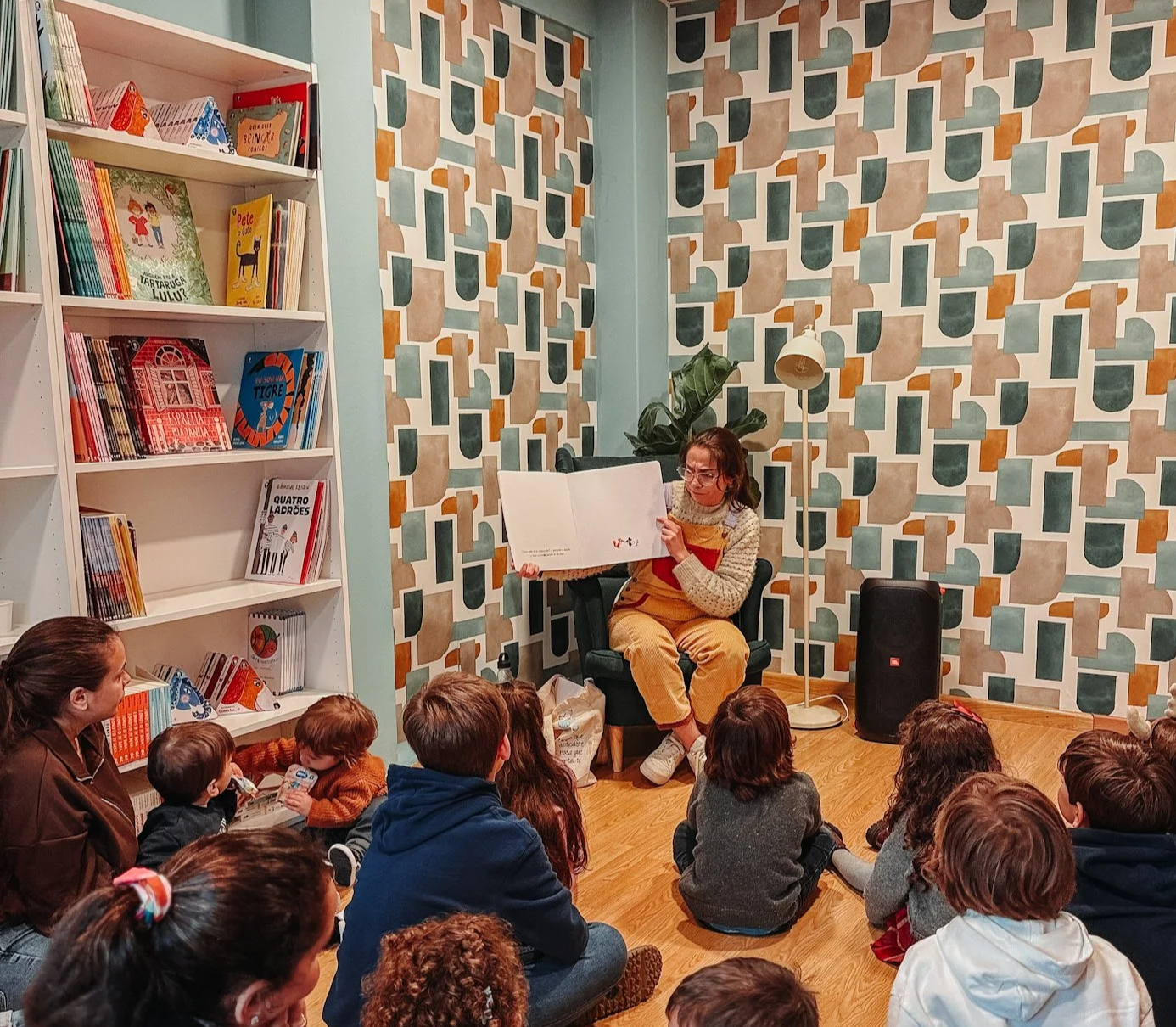 Mulher lendo livro para grupo de crianças sentado no chão em uma livraria ou biblioteca.