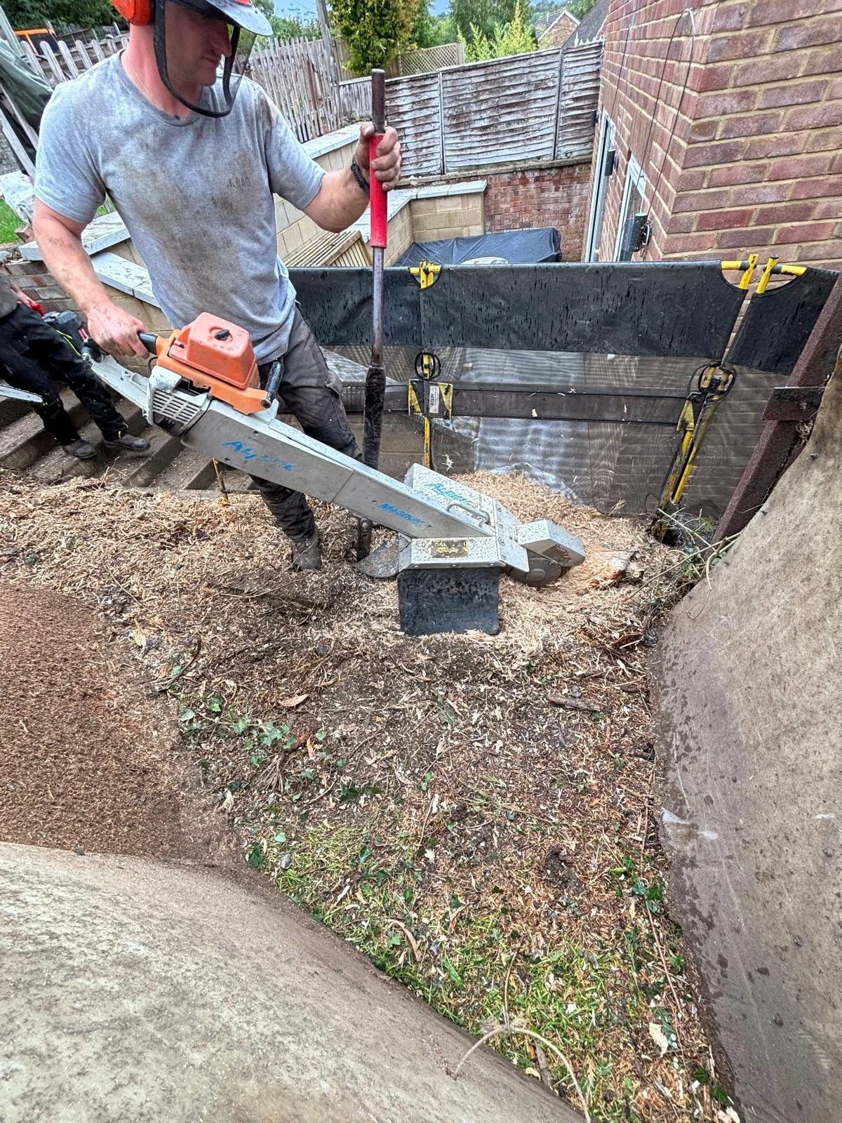A man operating a concrete cutting saw at a construction site near a brick wall.