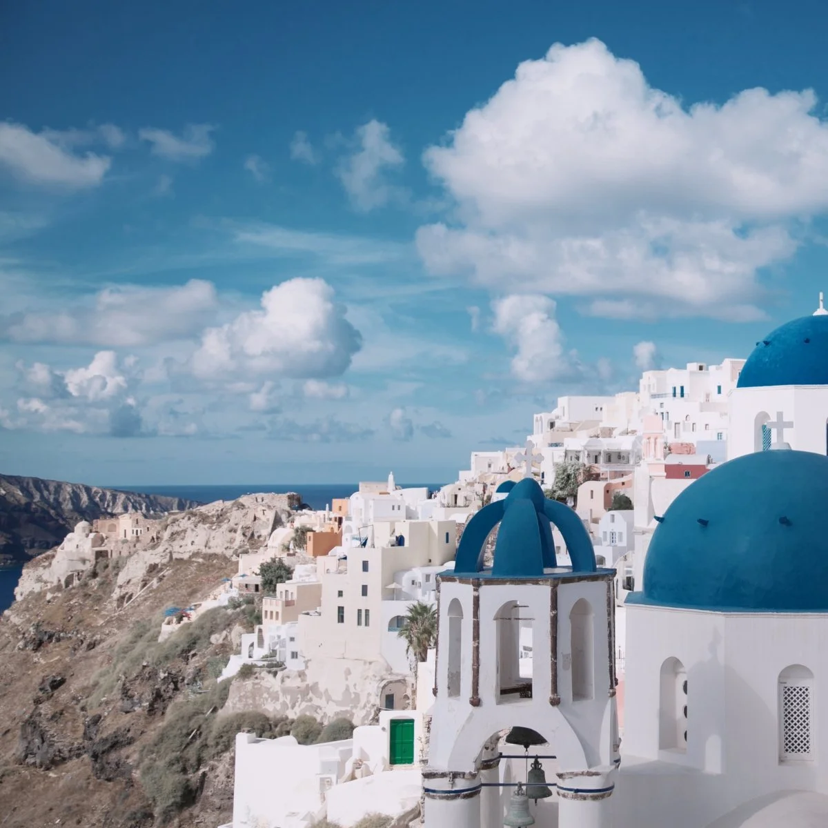 A scenic view of Santorini, Greece, featuring white buildings with blue domes against a partly cloudy sky.
