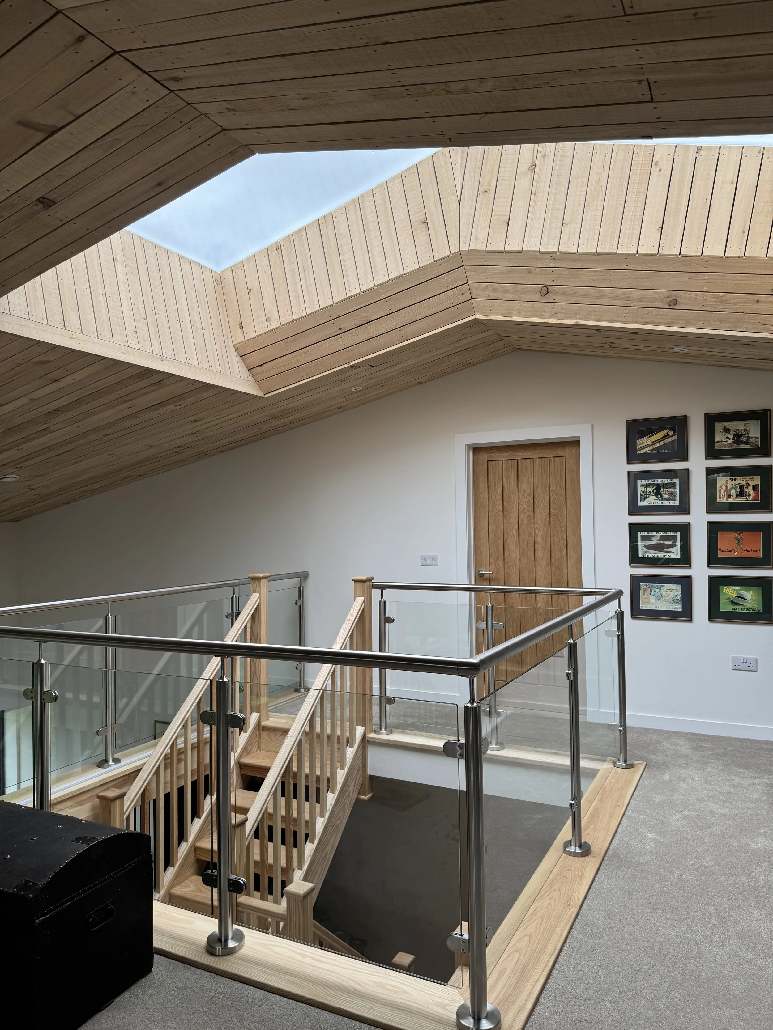 Interior view of a wooden-ceiling room with skylight, staircase with glass and wood railing, wooden door, and framed art.