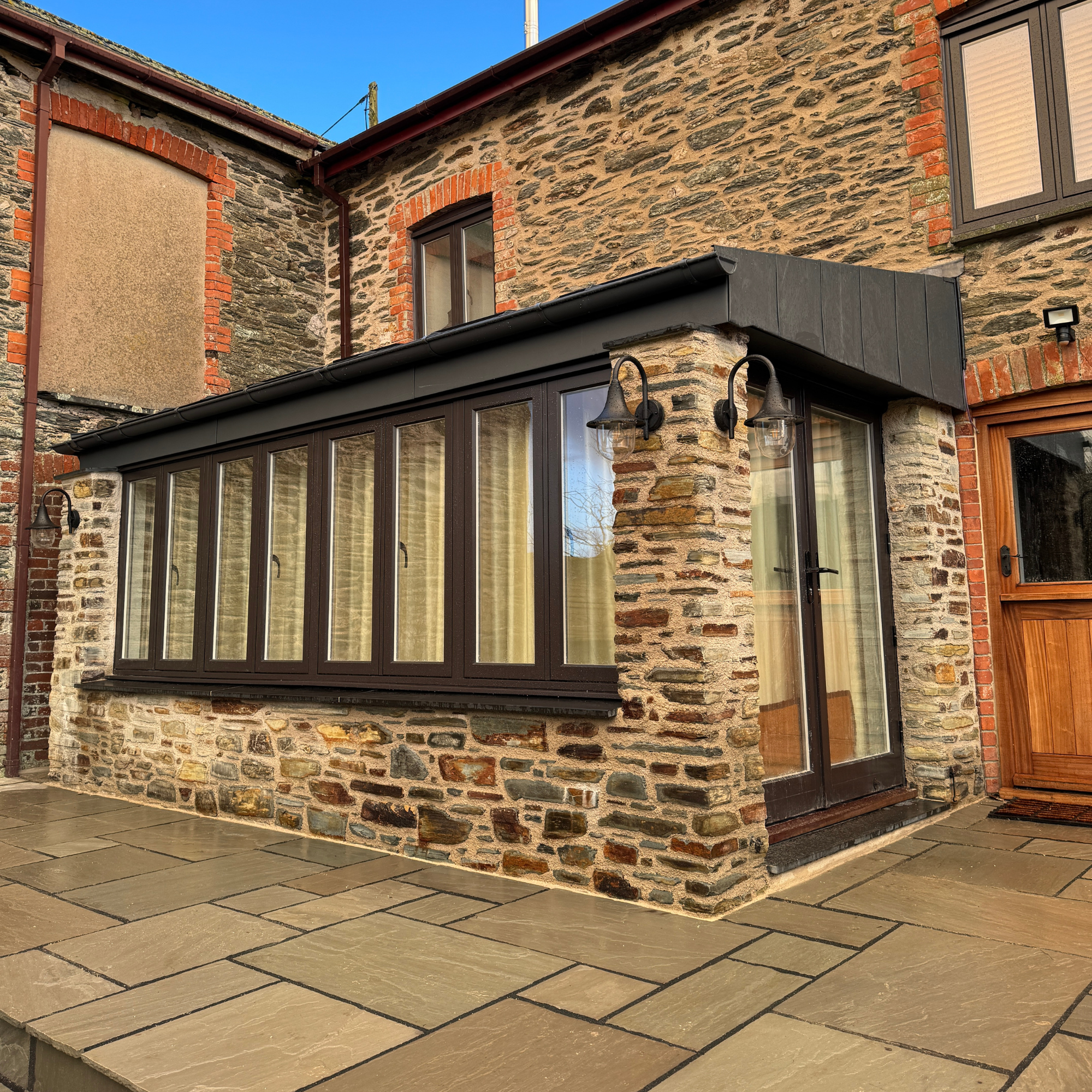 Back patio and home extension with stone walls, large windowed porch, and outdoor lighting fixtures.