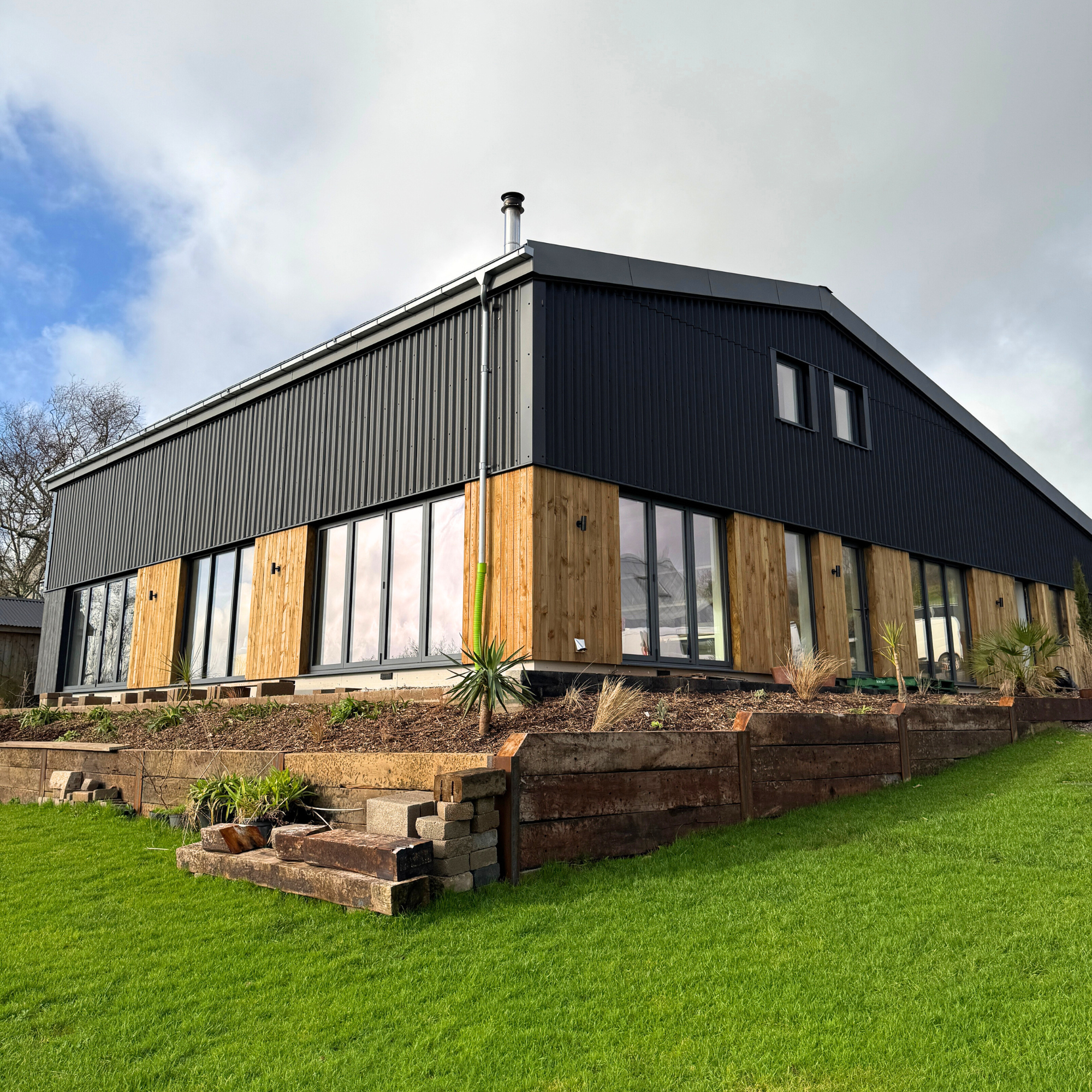 A huge two-story house with black metal panels and wooden exterior, large glass sliding doors.