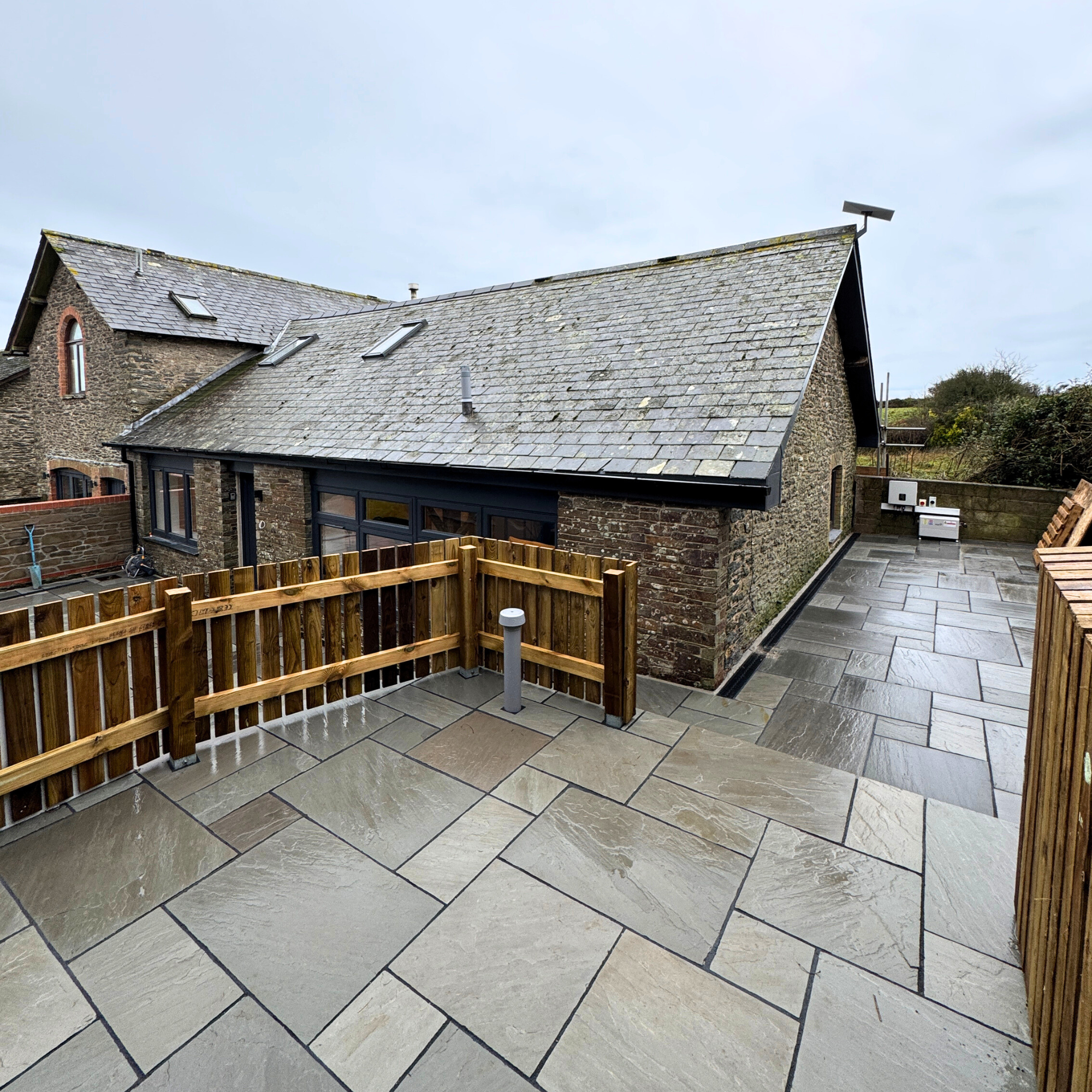 Photo of a roof of a brick house and patio area with stone flooring, wooden fencing.