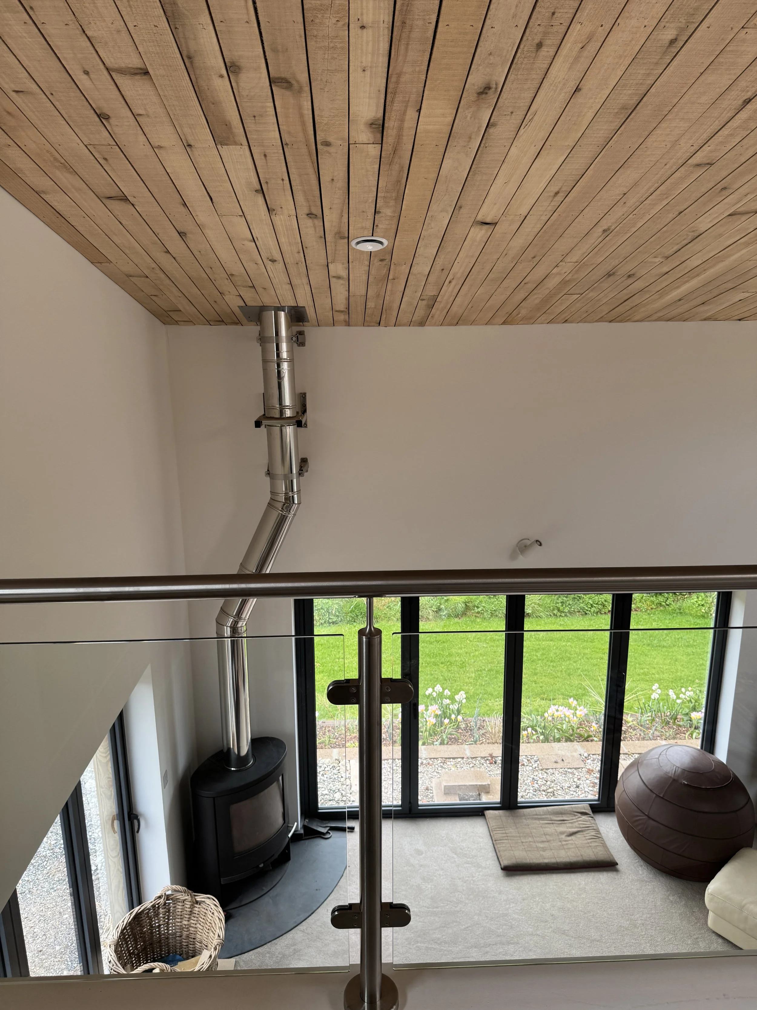 Interior view from upper level showing a wood stove with metal pipe, large glass sliding doors leading to a garden.