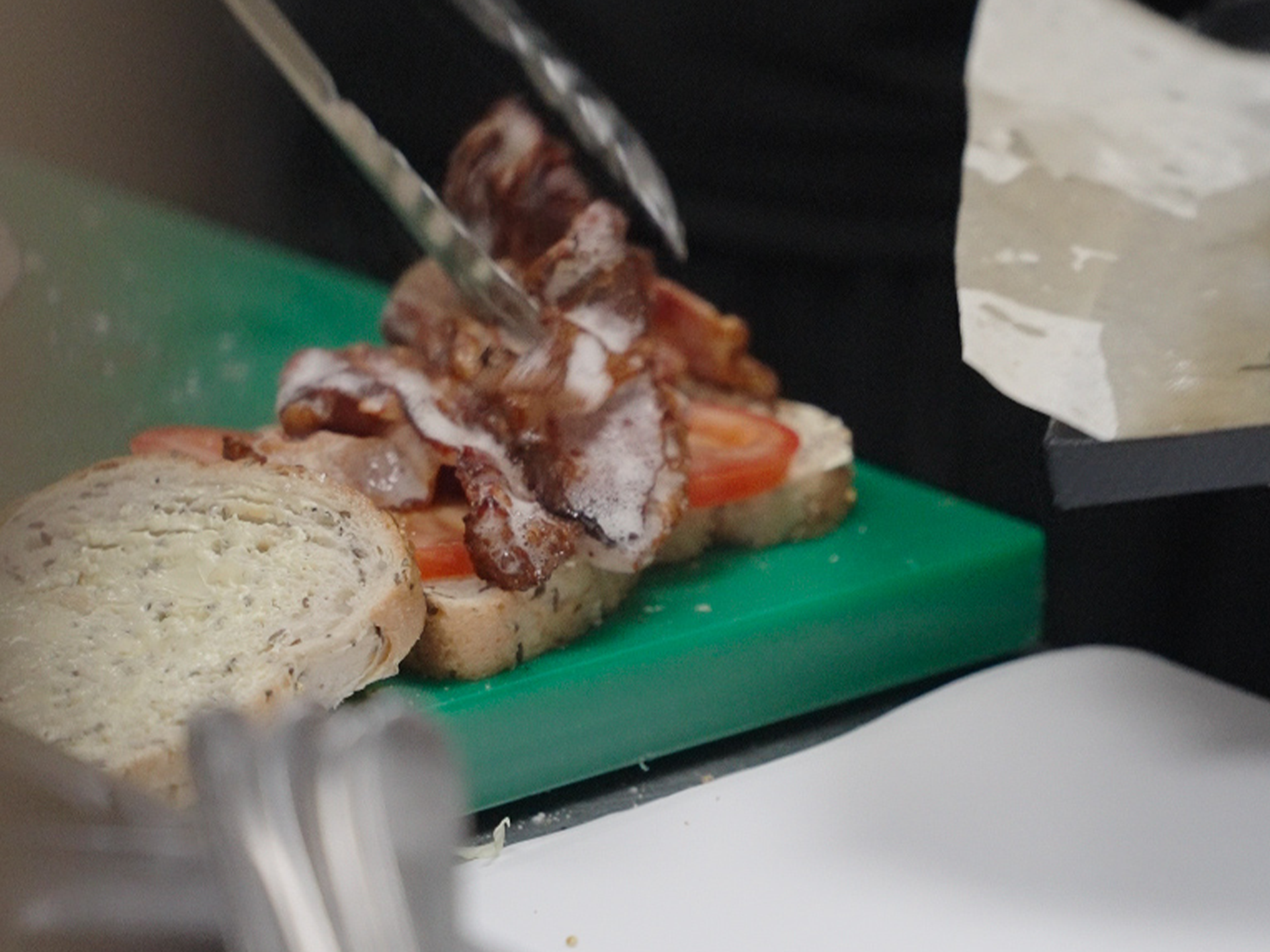 Sliced bread with bacon, tomato slices, and white sauce on a green cutting board.