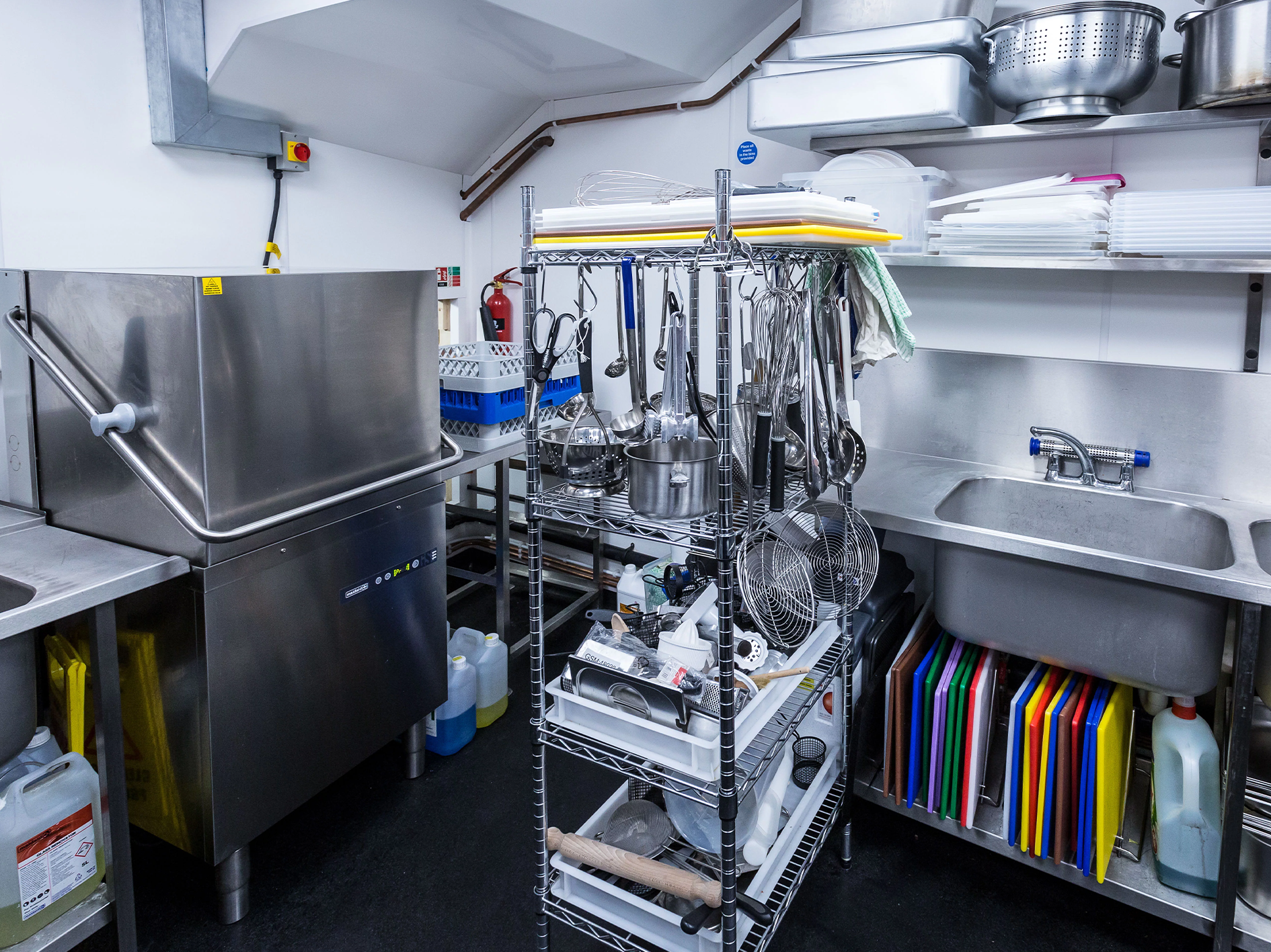 Commercial kitchen preparation area with various utensils, cutting boards, and cleaning supplies.