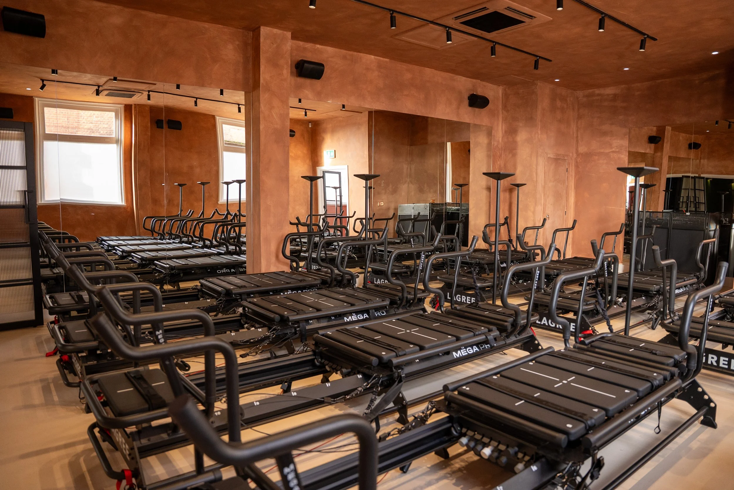 Indoor fitness studio with multiple rowing machines arranged in rows, large windows, and warm-toned walls.