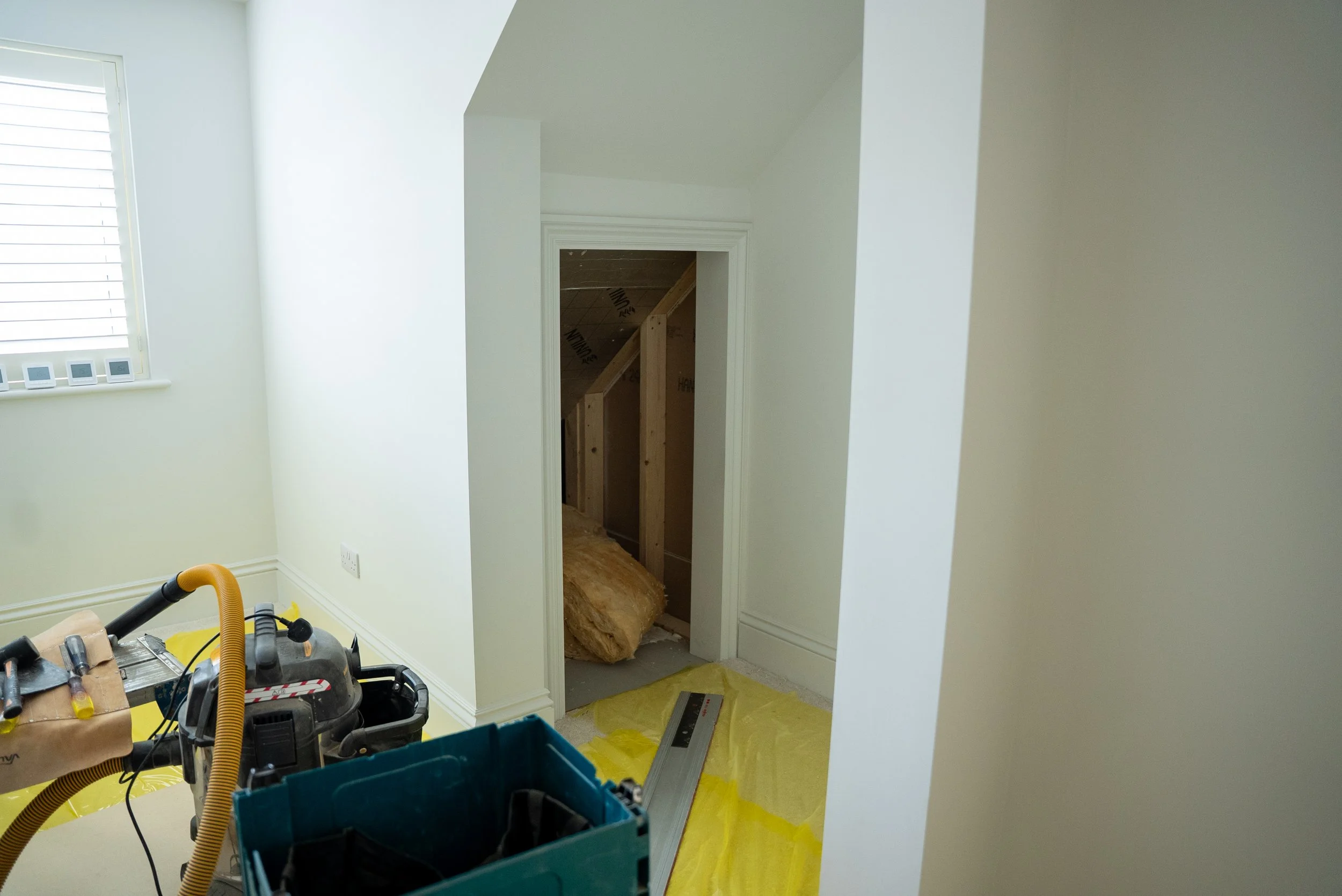 Interior of a house under construction, showing a doorway with some insulation and wooden framing visible inside.