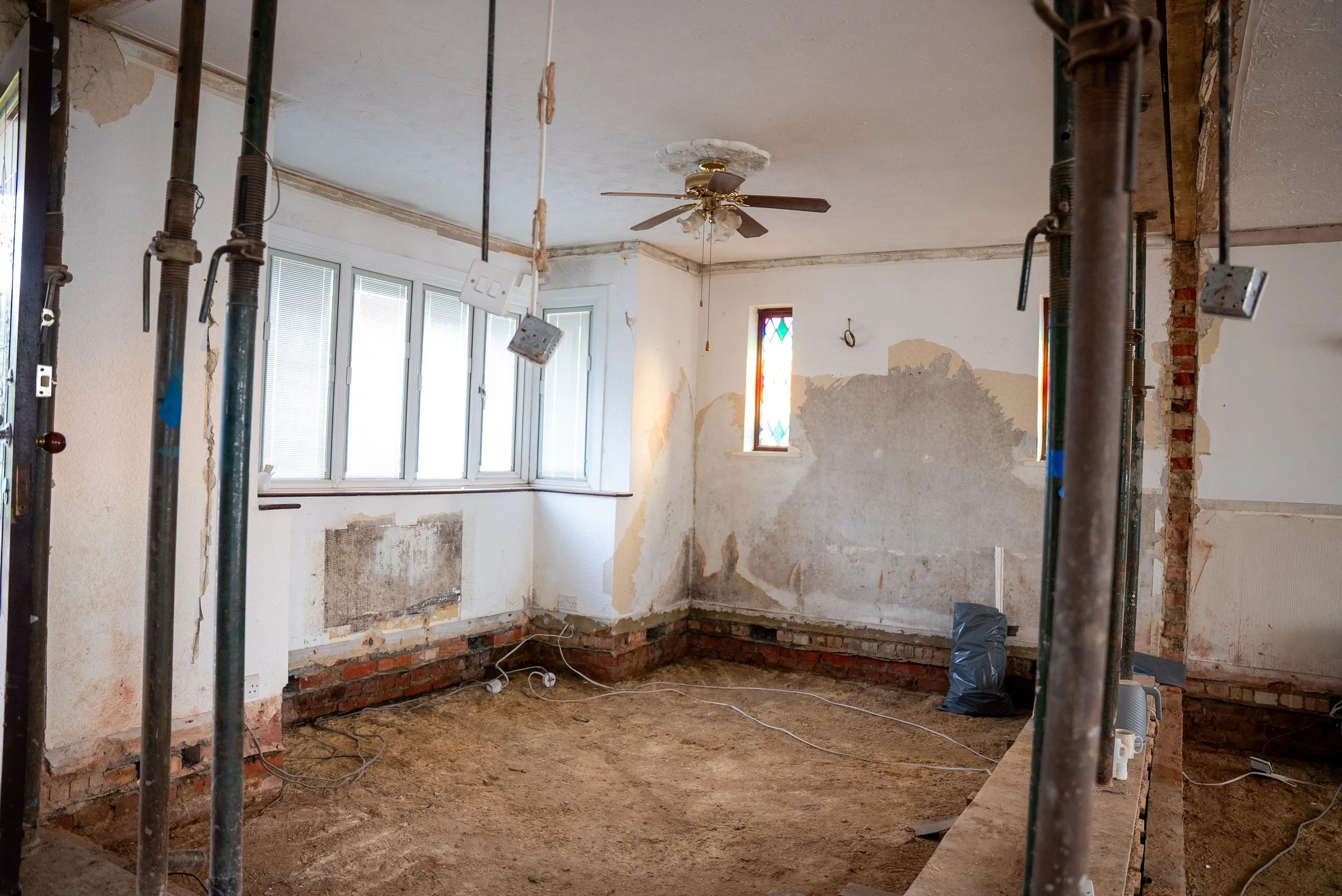 Room under renovation with exposed brick and drywall, scaffolding, a ceiling fan, and stained glass windows.