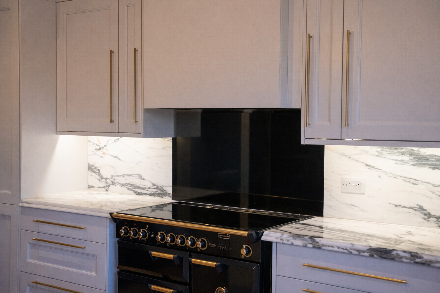 A modern kitchen with white cabinets, gold handles, marble countertops, and a black stove with gold knobs.