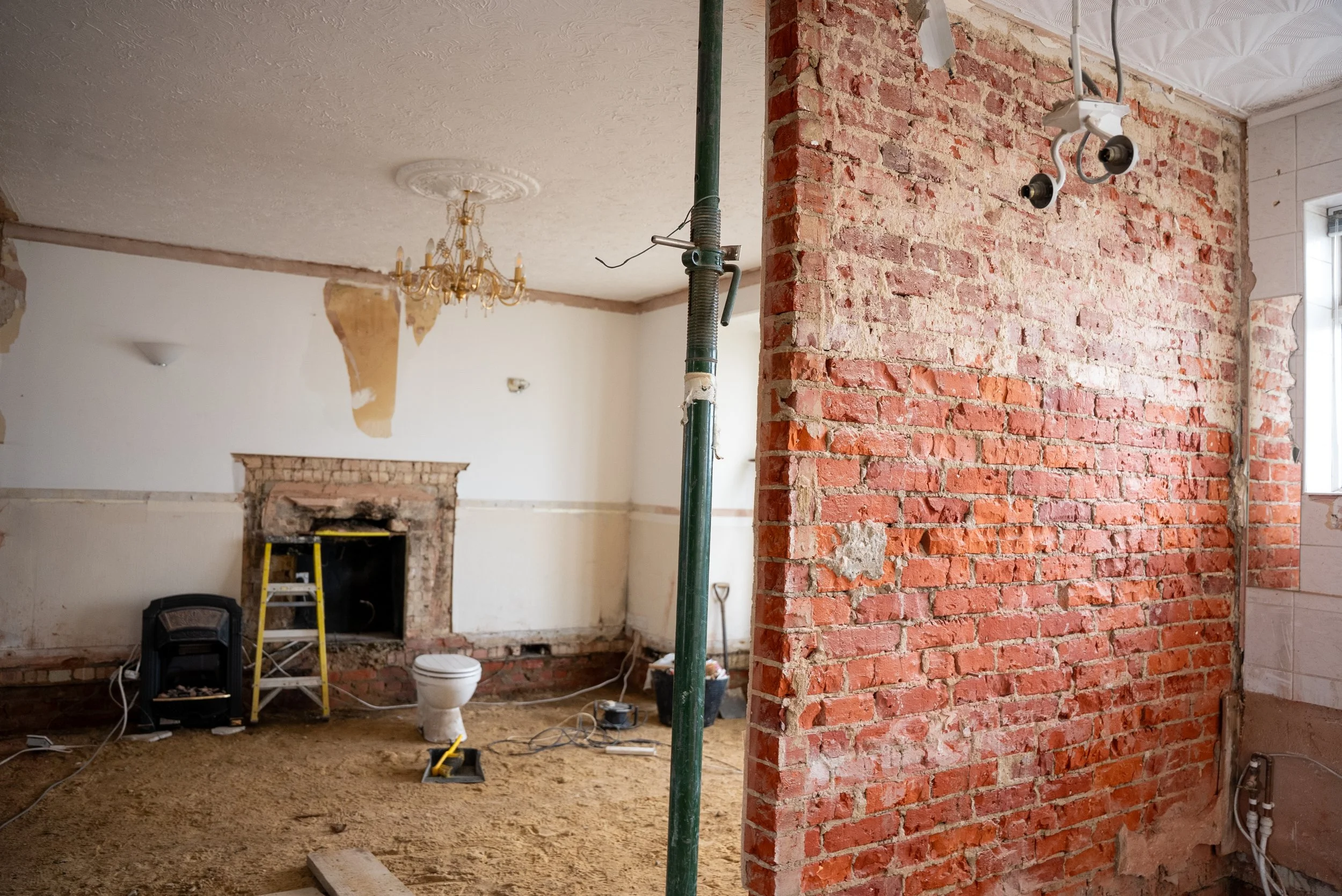 Interior under renovation with exposed brick walls, construction tools, and a partially demolished fireplace