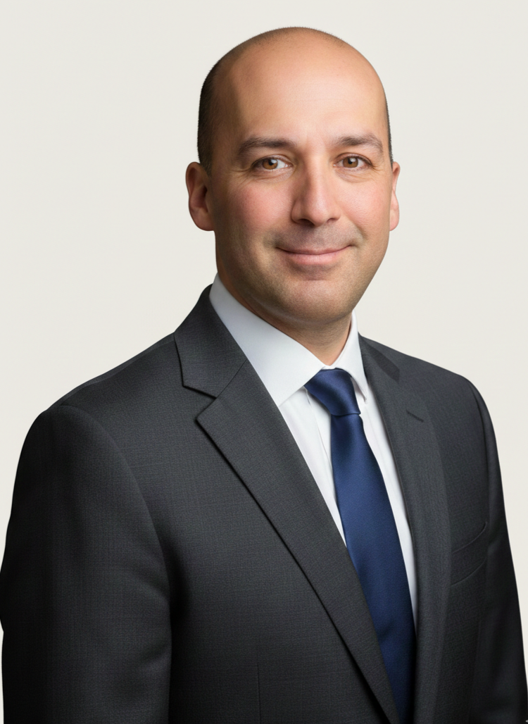 A man in a dark suit, white shirt, and navy blue tie smiling against a plain light background.