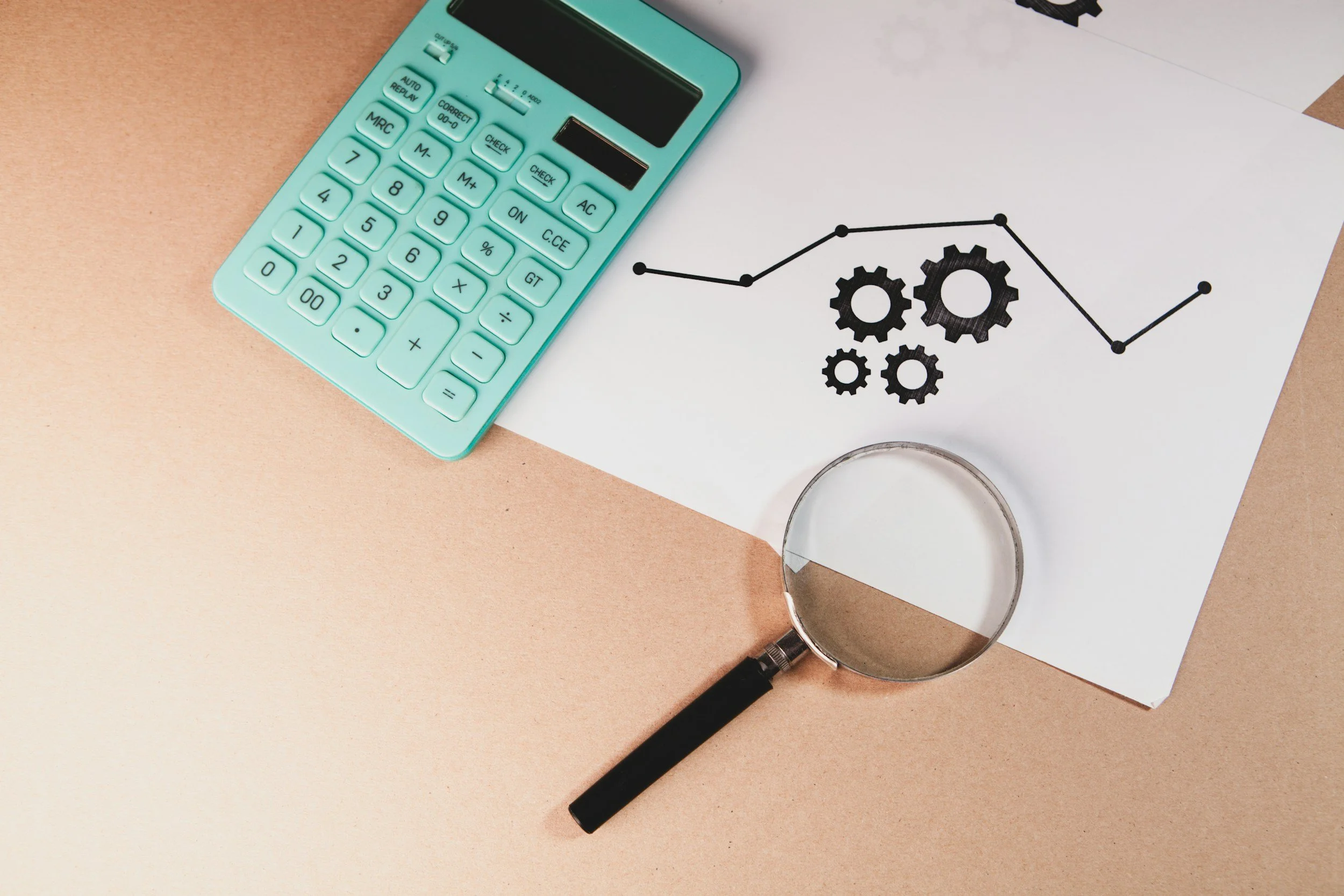Green calculator, magnifying glass, and a piece of paper with a line graph and gear illustrations on a split beige and white background.