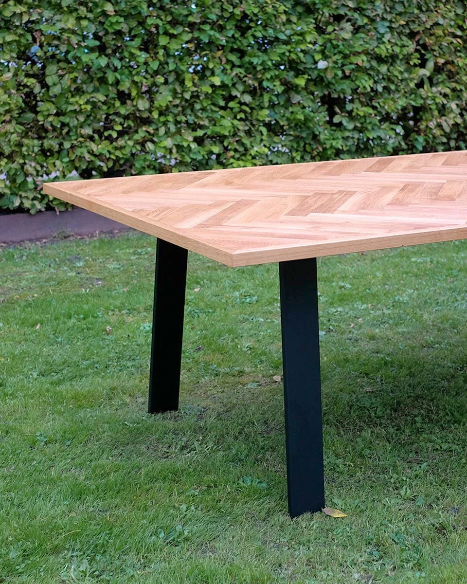 Ein rechteckiger Holztisch auf grünem Gras mit einem Busch im Hintergrund.