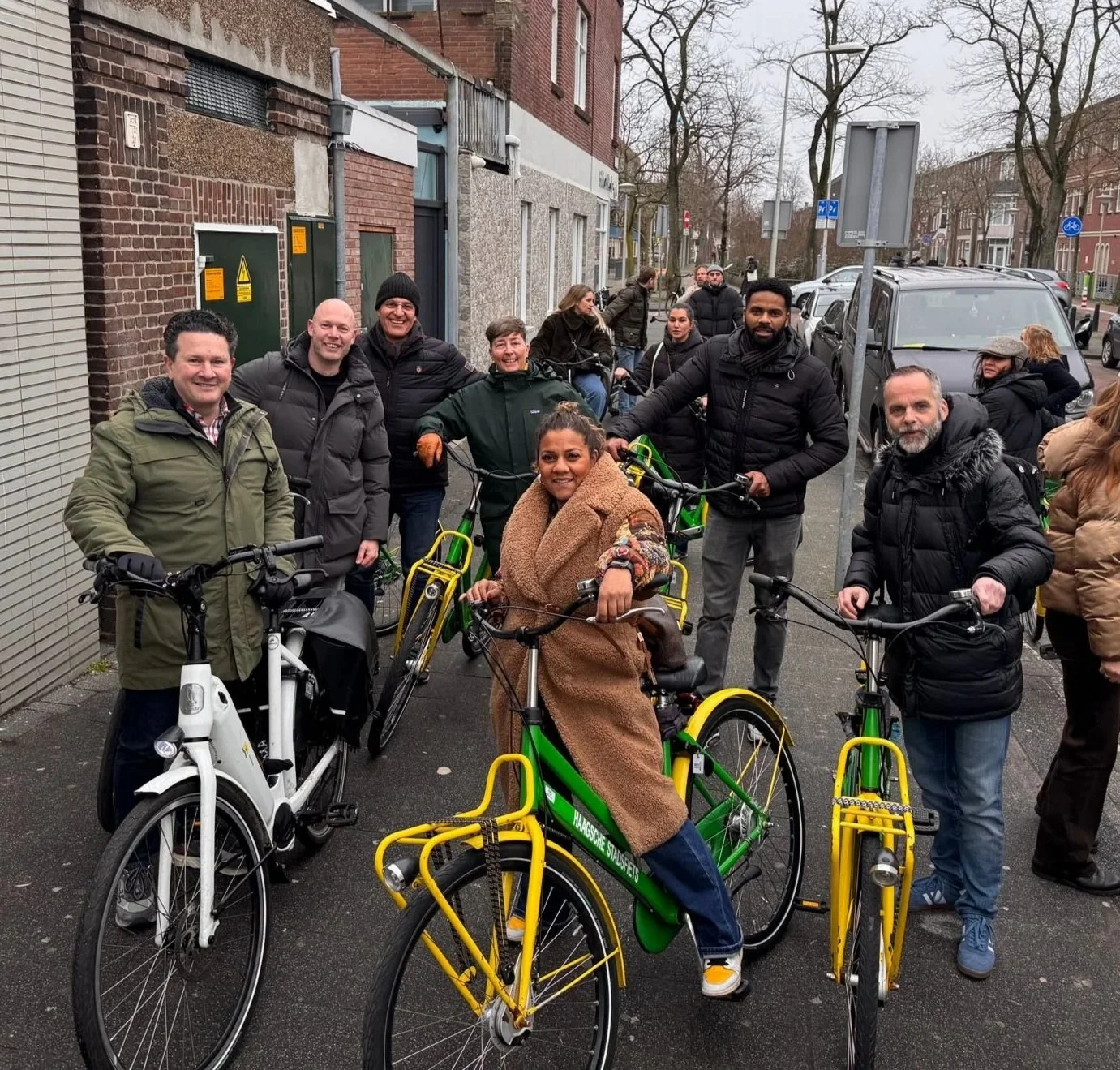 Groep mensen met fietsen op straat tijdens een bijeenkomst of evenement, allemaal gekleed in winterkleding.