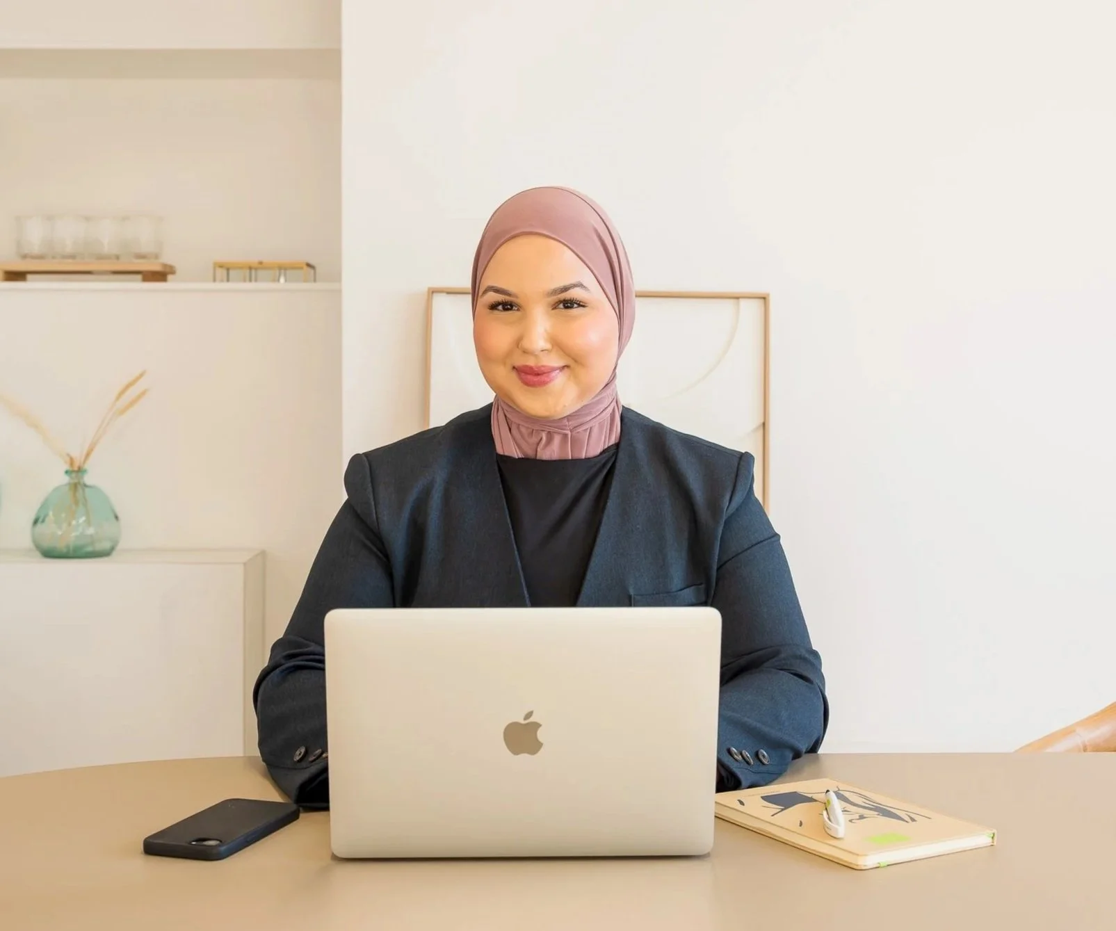 Vrouw met hoofddoek werkt achter laptop in kantoor.