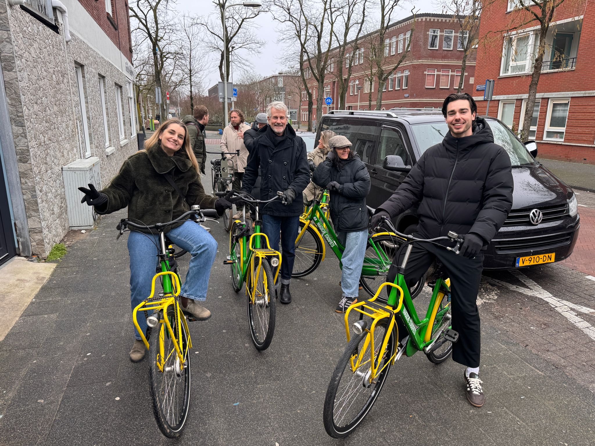 Groep mensen met fietsen op straat in een woonwijk, lachend en in gesprek.