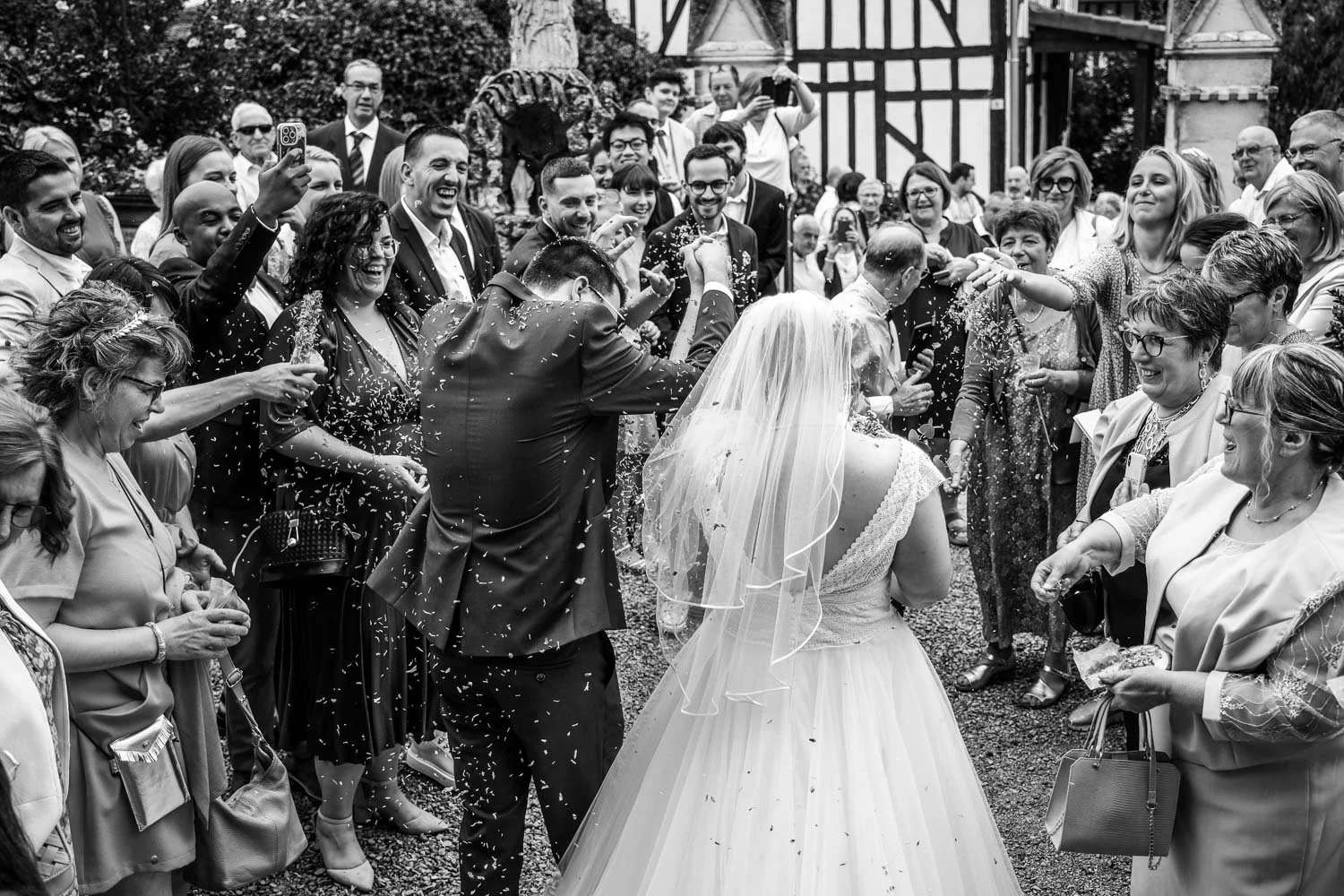 Un mariage avec des personnes célébrant la mariée sous la pluie de confettis devant une bâtisse en style traditionnel.