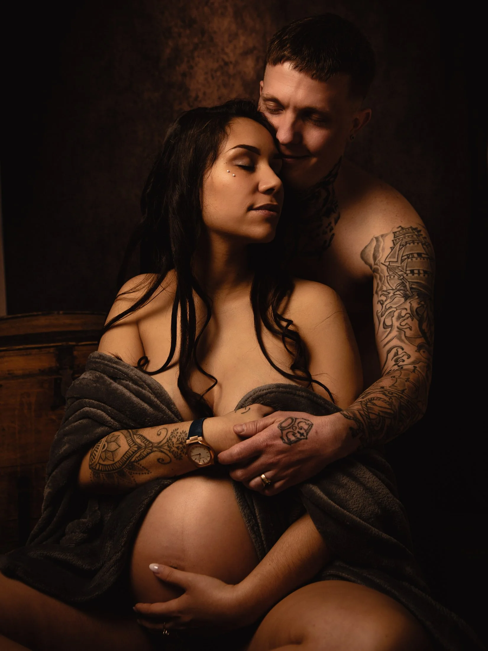 Portrait de couple de futurs parents enlacés dans une ambiance aux couleurs chaudes, en studio. 