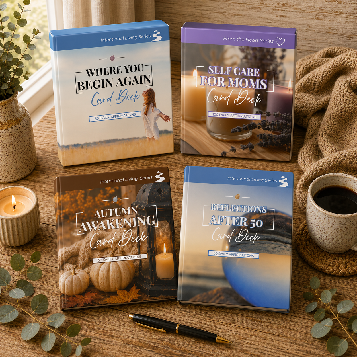 Four affirmation card decks arranged on a wooden table with candles, a mug of coffee, and eucalyptus leaves. The decks are titled 'Where You Begin Again,' 'Self Care for Moms,' 'Autumn Awakening,' and 'Reflections After 50.'