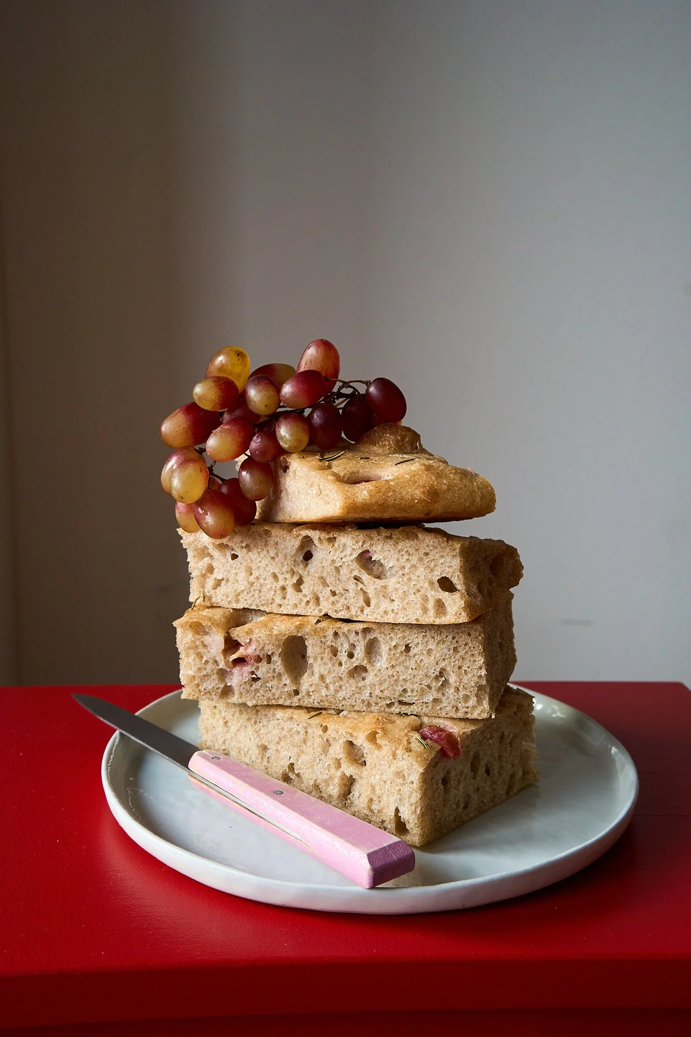 Food Styling von italienischem Focaccia mit Weintrauben auf einem roten Tisch.