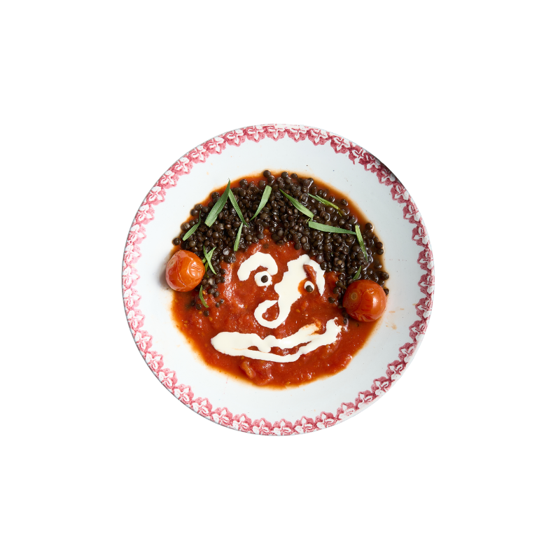 Kinderernährung, Ernährungsbildung für Kitas: Ein Teller mit Linsensuppe, dekoriert mit Tomaten und Frühlingszwiebeln, das Ganze ist kunstvoll angerichtet, um ein lachendes Gesicht zu formen.