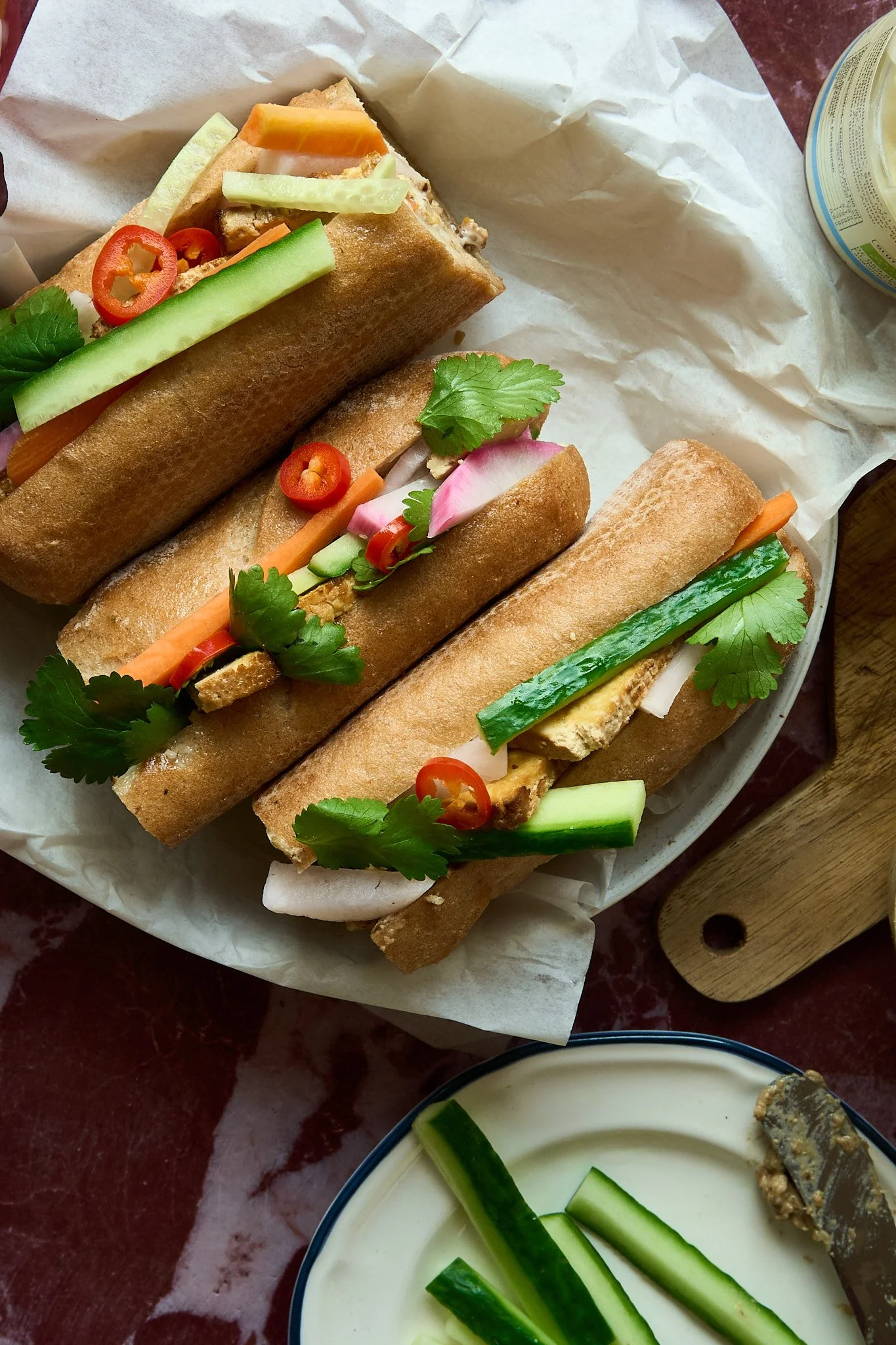 Food Styling für Markttag Kochbuch: Vier vietnamesische Baguette-Sandwiches mit frischen Kräutern und Gemüse, serviert auf Papier auf einem hölzernen Tisch.