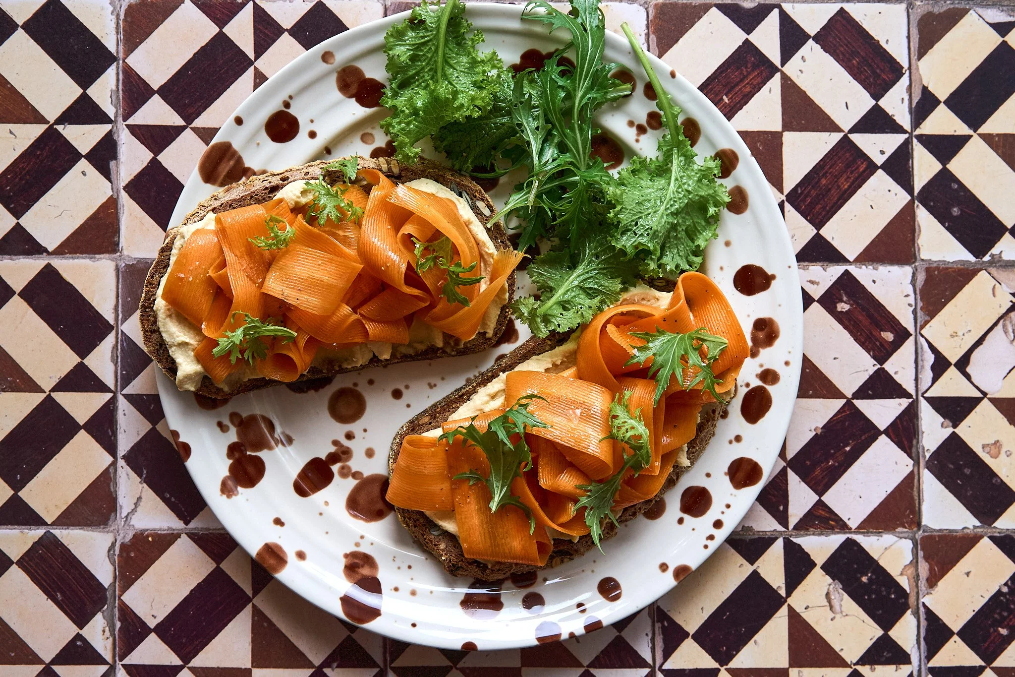 Rezeptentwicklung und Food Styling von Kochbuchautorin: Brot mit Hummus, eingelegten Karottenscheiben und frischer grün Salat auf einem weißen Teller