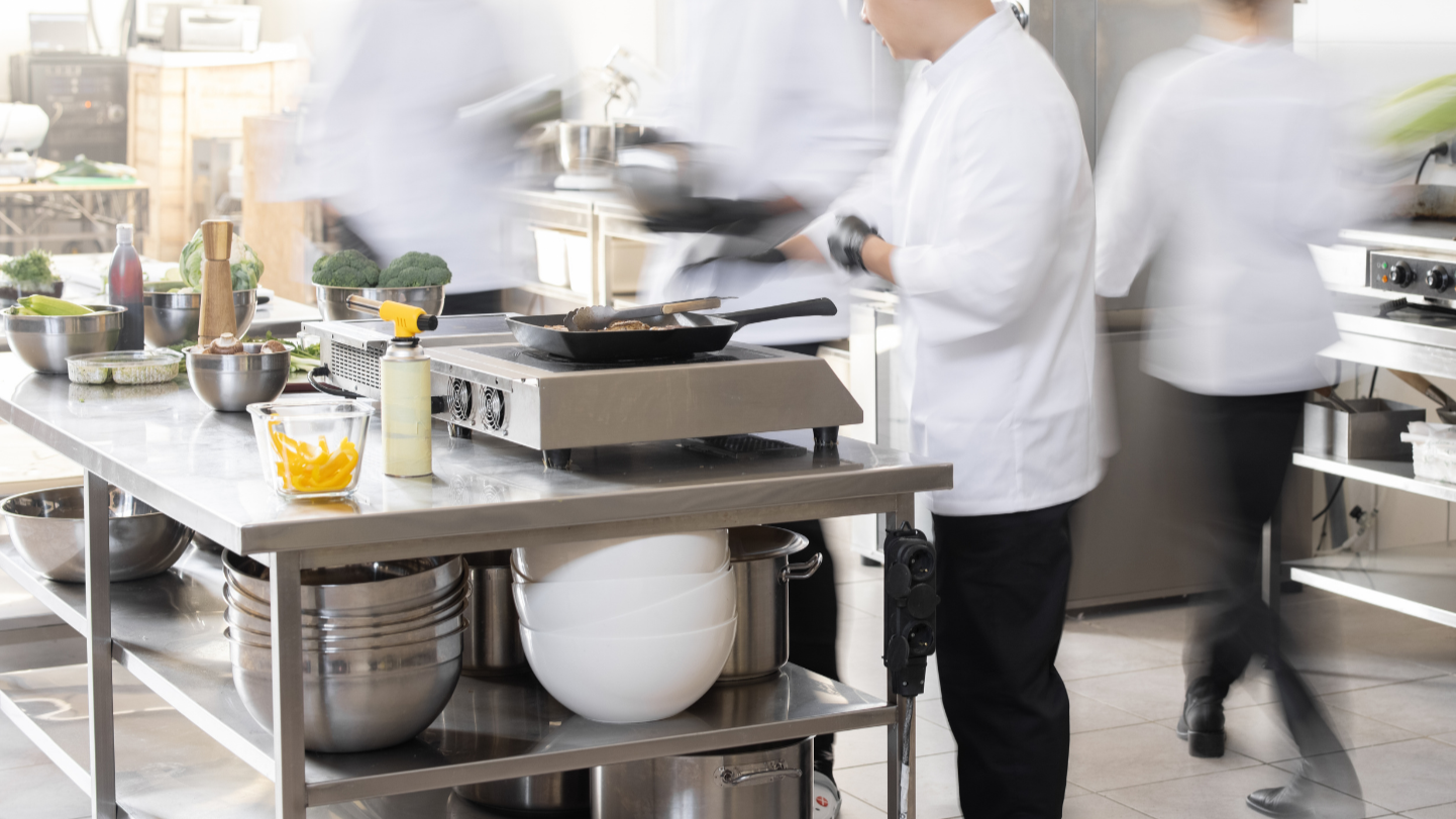 Cuisiniers en action dans une cuisine professionnelle, préparant des plats avec des légumes frais sur une table en acier inoxydable.
