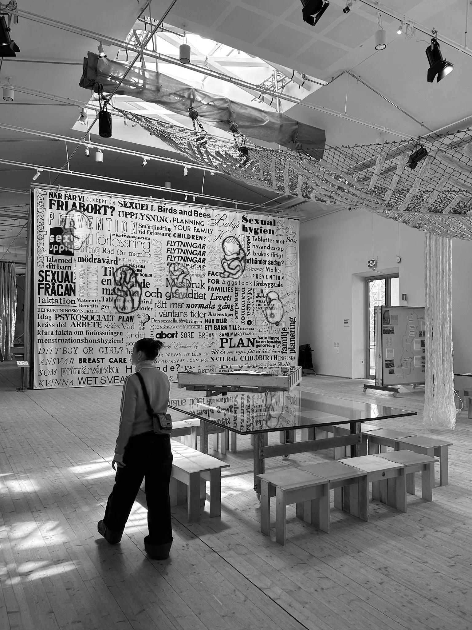 Ein Museumsraum mit einer Wand voller Textwände in schwedischer Sprache, mehreren Sitzbänken und einer Frau, die nach vorne schaut.