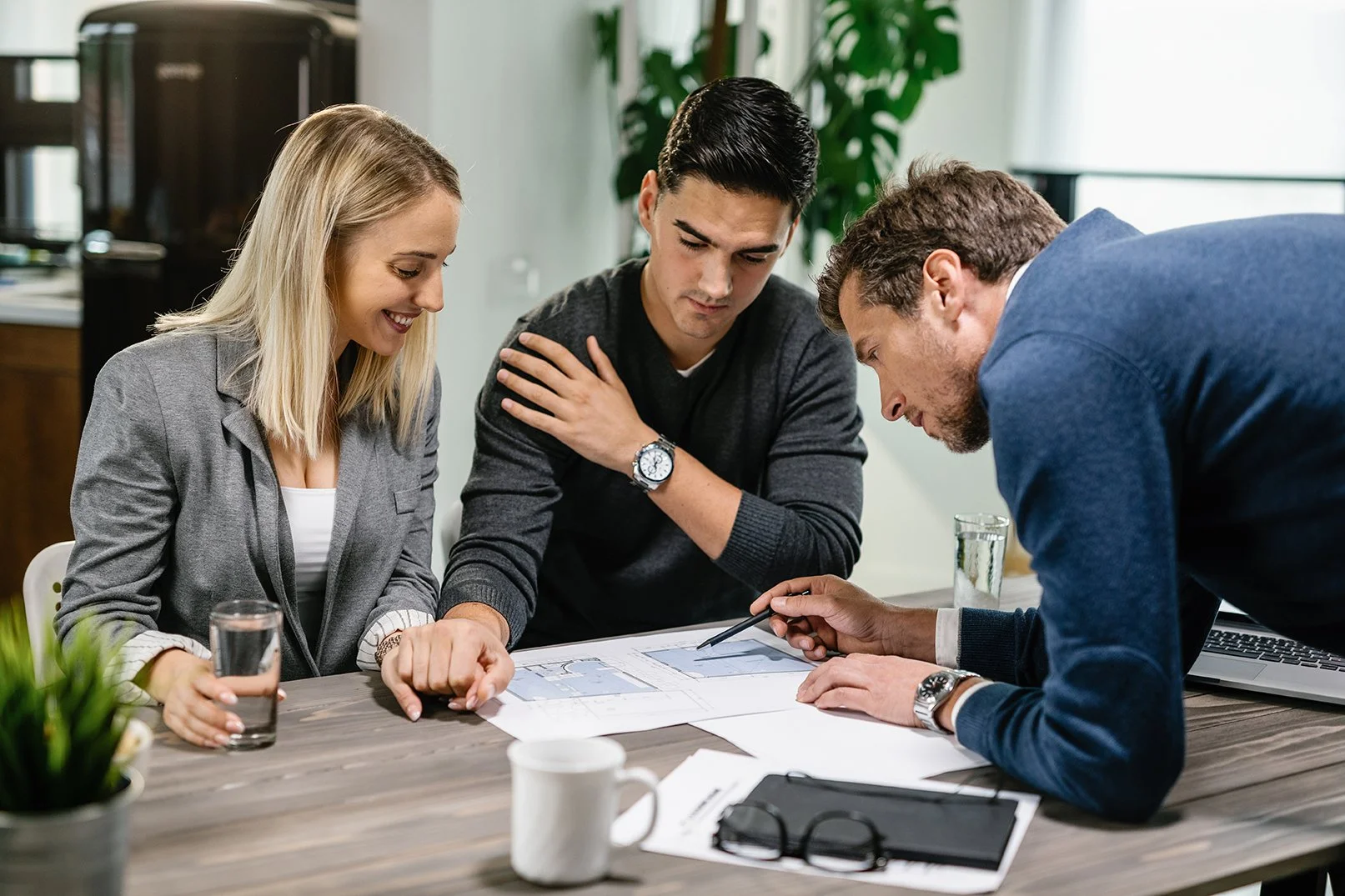Three people in business attire gathered around a conference table examining documents and discussing.