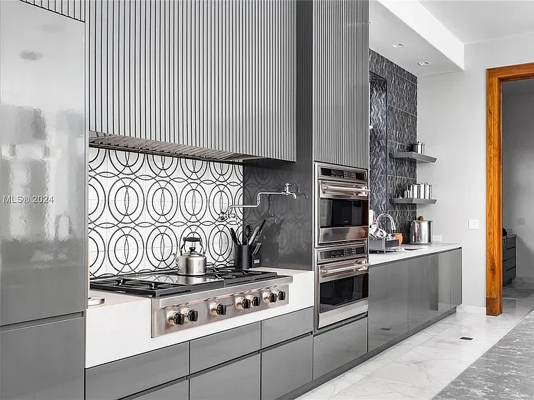 Modern kitchen with gray cabinets, stainless steel appliances, patterned backsplash, and open shelving with kitchenware.