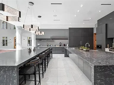 Modern kitchen with white and gray color scheme, island with barstools, pendant lights, and built-in appliances.