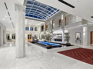 Luxurious hotel lobby with a glass ceiling, marble floors, a central water feature, and elegant decor.