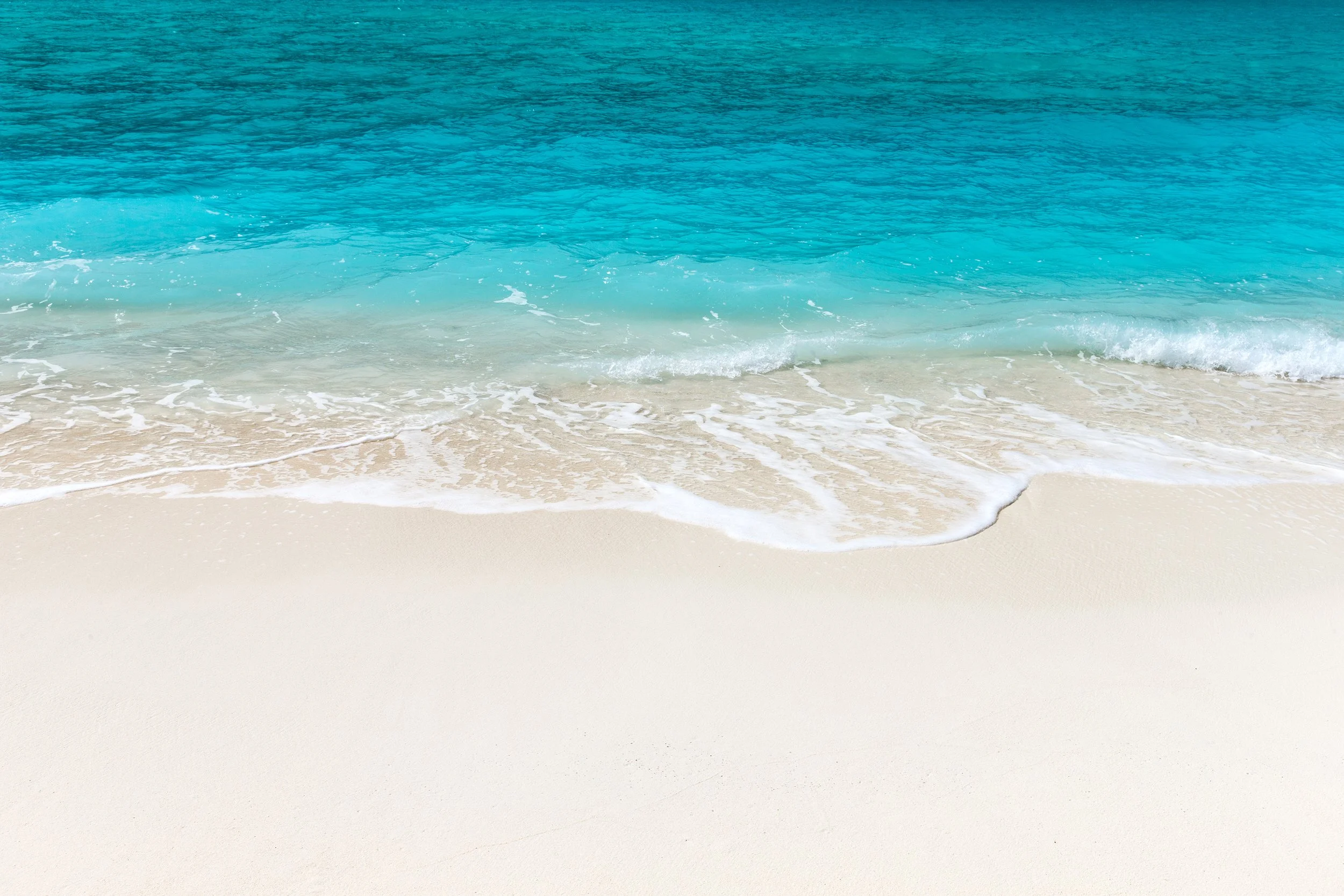 Calm turquoise ocean waves gently lapping onto a sandy beach.